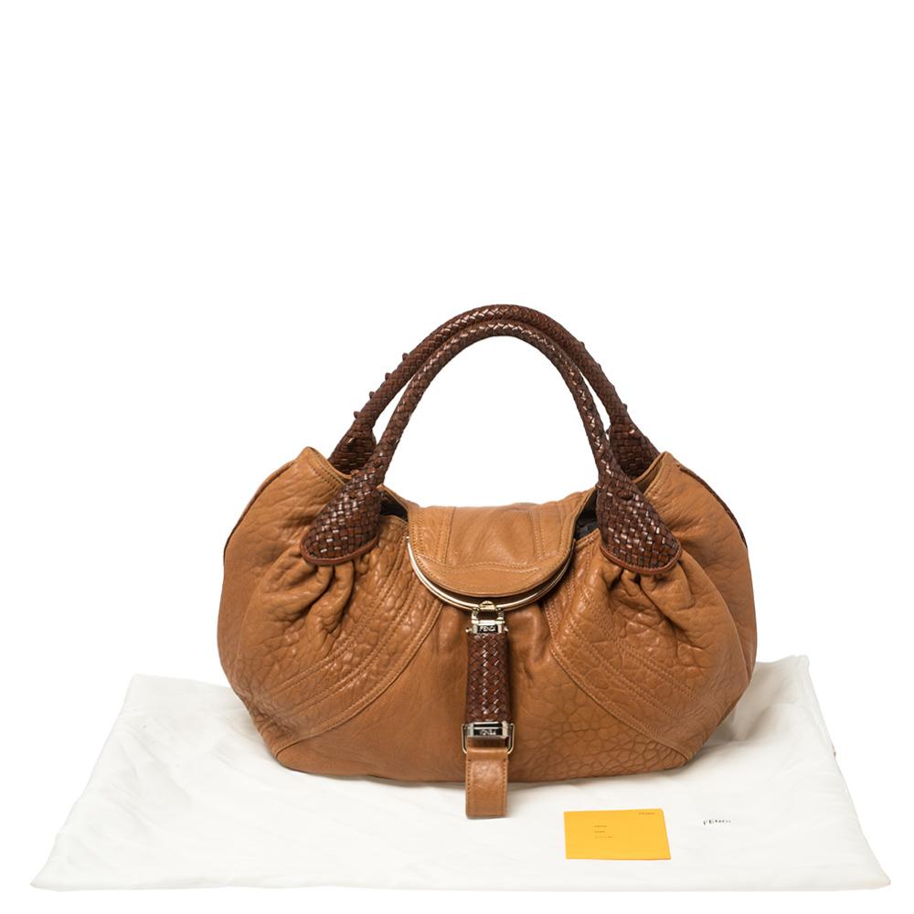 Amp up your style for the season with this tan spy hobo made of Nappa leather. The canvas lining of this Fendi bag makes it versatile and sturdy. It features woven rolled leather handles and a flap with a magnetic closure. It is finished with