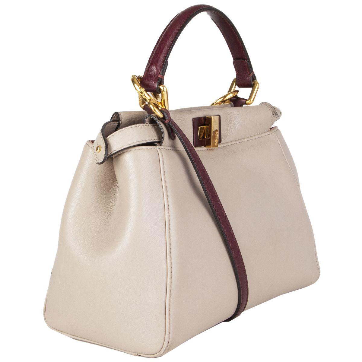 Fendi 'Peekaboo Mini' in light taupe nappa leather with burgundy handle and shoulder strap featuring gold-tone hardware. Opens with turn-lock to a dual-compartment interior with one zipper pocket and slip pocket in the middle. Lined in baby pink