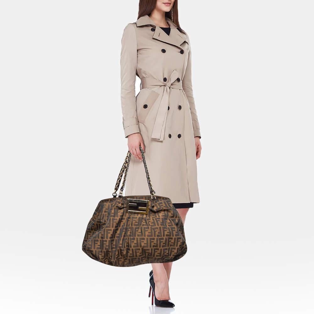 This beautiful Fendi bag has been crafted in brown monogrammed Zucca canvas. It features signature logo buckle detailing at the pleated front in gold tone. The double straps are in woven pattern and look truly stunning. The open top reveals a fabric
