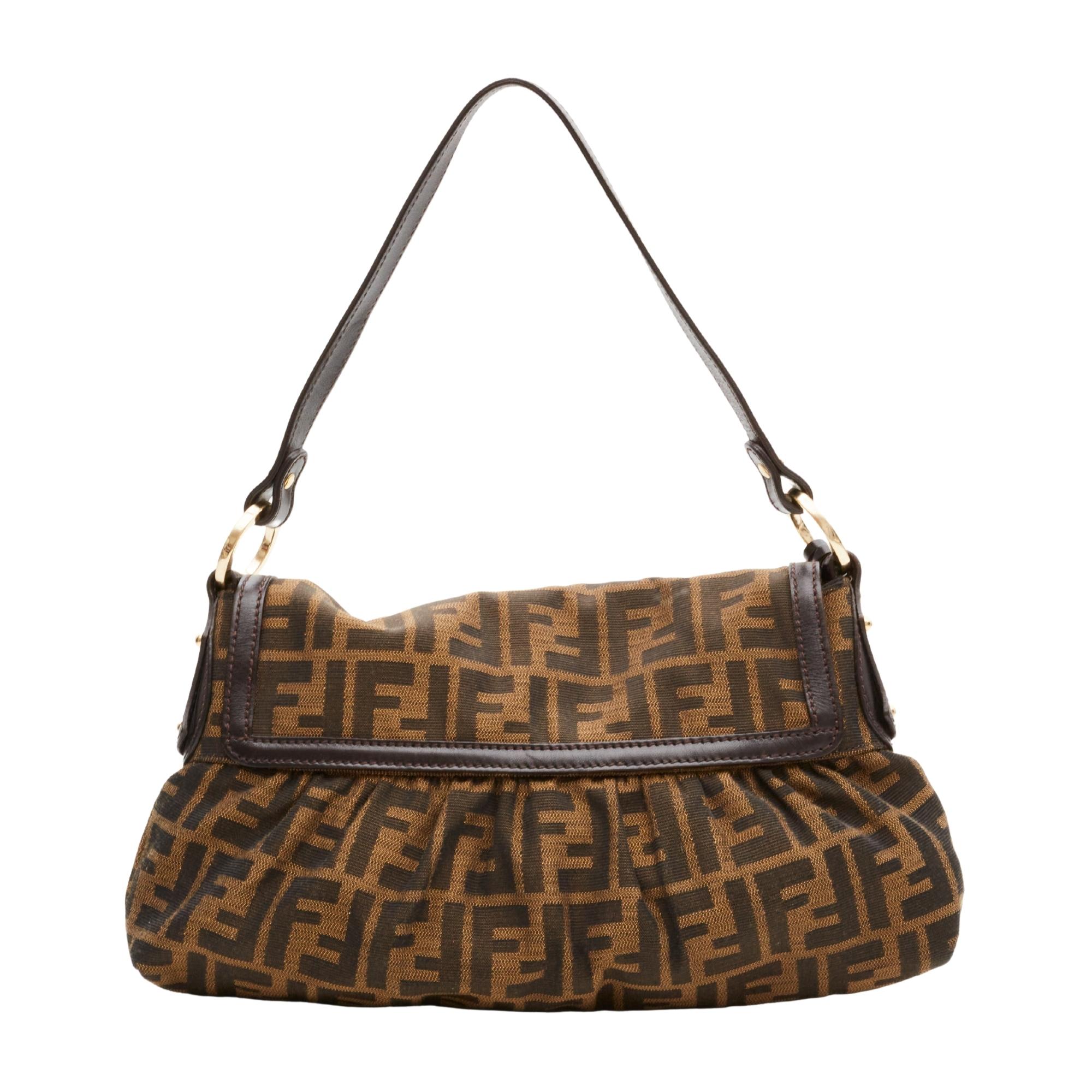 This bag is made with classic Fendi monogram Zucca print on brown canvas with brown leather finishes. The bag features a flat leather shoulder strap attached by gold tone hardware circular links, a hanging logo charm at front, a front flap, and