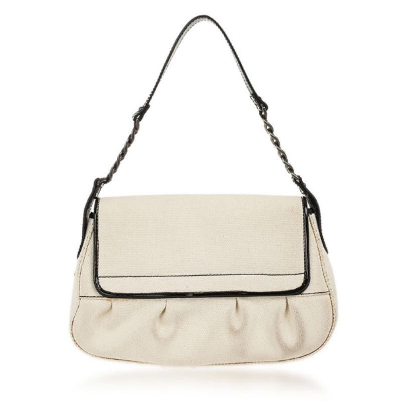 This Fendi B Bag is made from white canvas and beautifully contrasted with patent black leather trim. It is accented with large buckles with logo prongs, a single leather and chain link shoulder strap and gold-tone hardware. The interior is lined