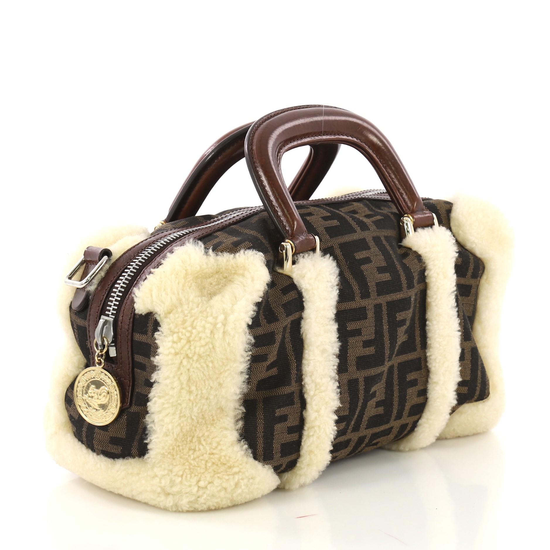 This Fendi Vintage Convertible Boston Bag Zucca Canvas and Shearling Medium, crafted in brown zucca canvas and shearling, features dual leather handles and gold and silver-tone hardware. Its zip closure opens to a brown fabric interior. 

Condition: