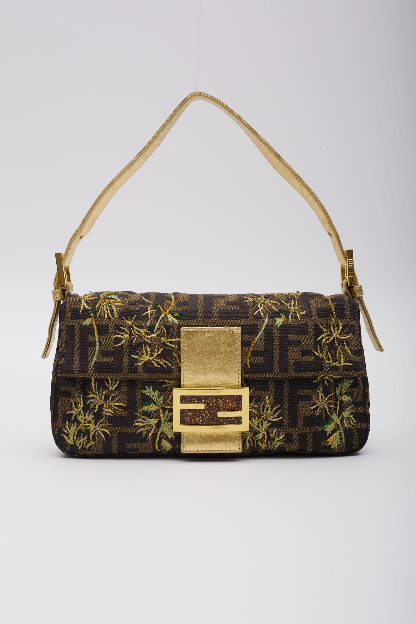 This vintage Fendi Baguette bag is crafted from brown canvas adorned with the iconic black monogram Zucca print and intricate floral embroidery. The bag features gold leather finishes and details, accompanied by gold-tone hardware. It includes a