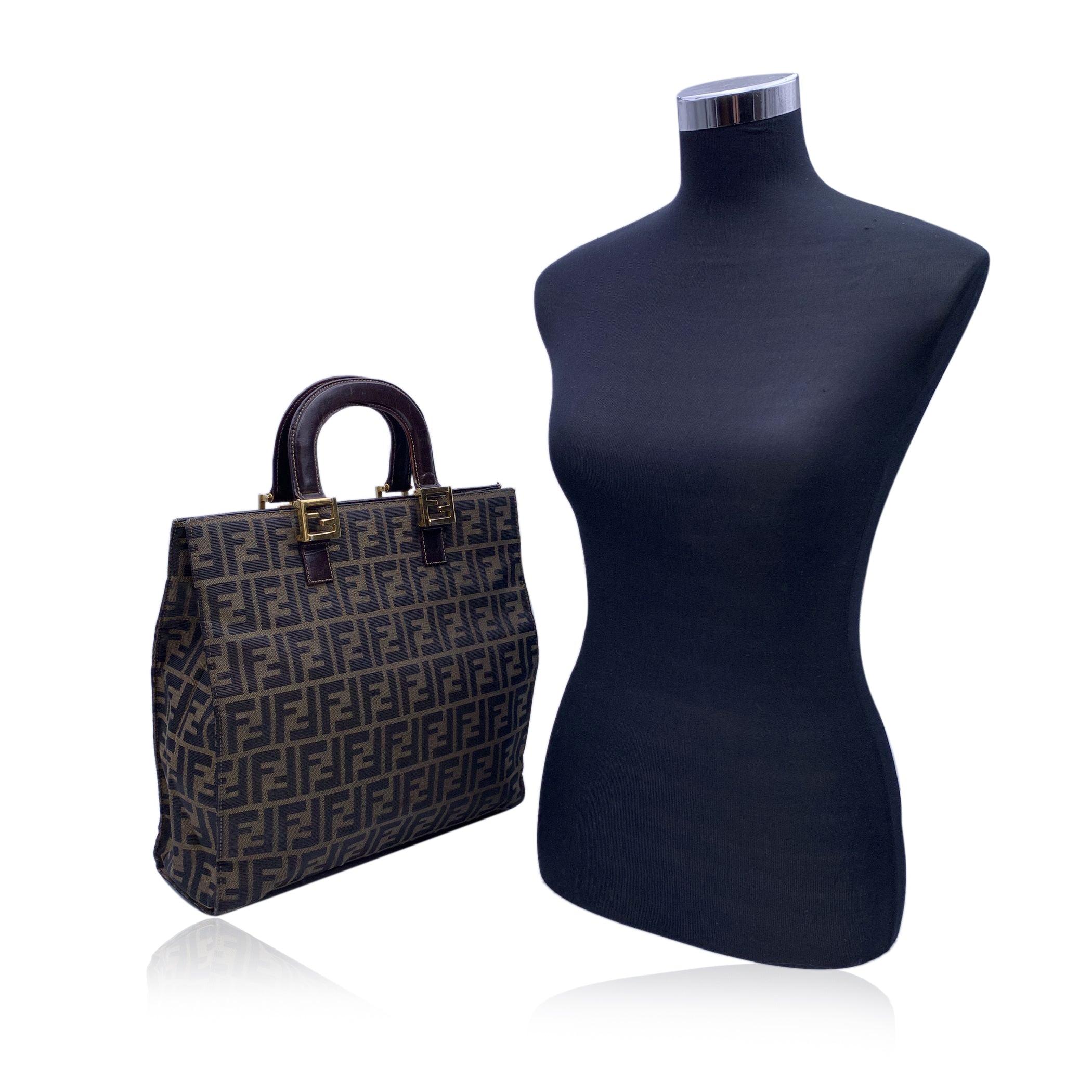 Vintage Fendi tote bag crafted in black and tobacco monogram Zucca canvas with brown genuine leather handles. Magnetic button closure on top. Gold metal FF - FENDI logo hardware. 1 side zip pocket inside. 'Fendi - Made in Italy' tag inside.