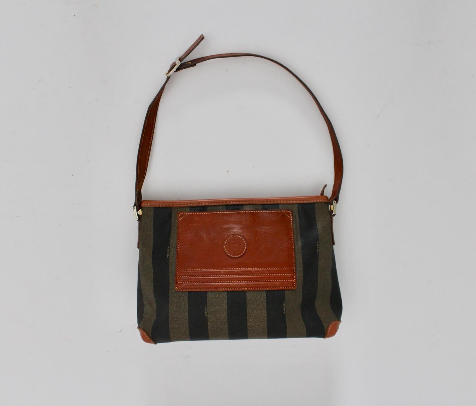 This vintage shoulder bag by Fendi shows a coated canvas surface with leather details.
Its zip closure opens a black lining with a side pocket, also to open with a zip.
The shoulder bag shows a preloved fair condition with signs of age and use. A