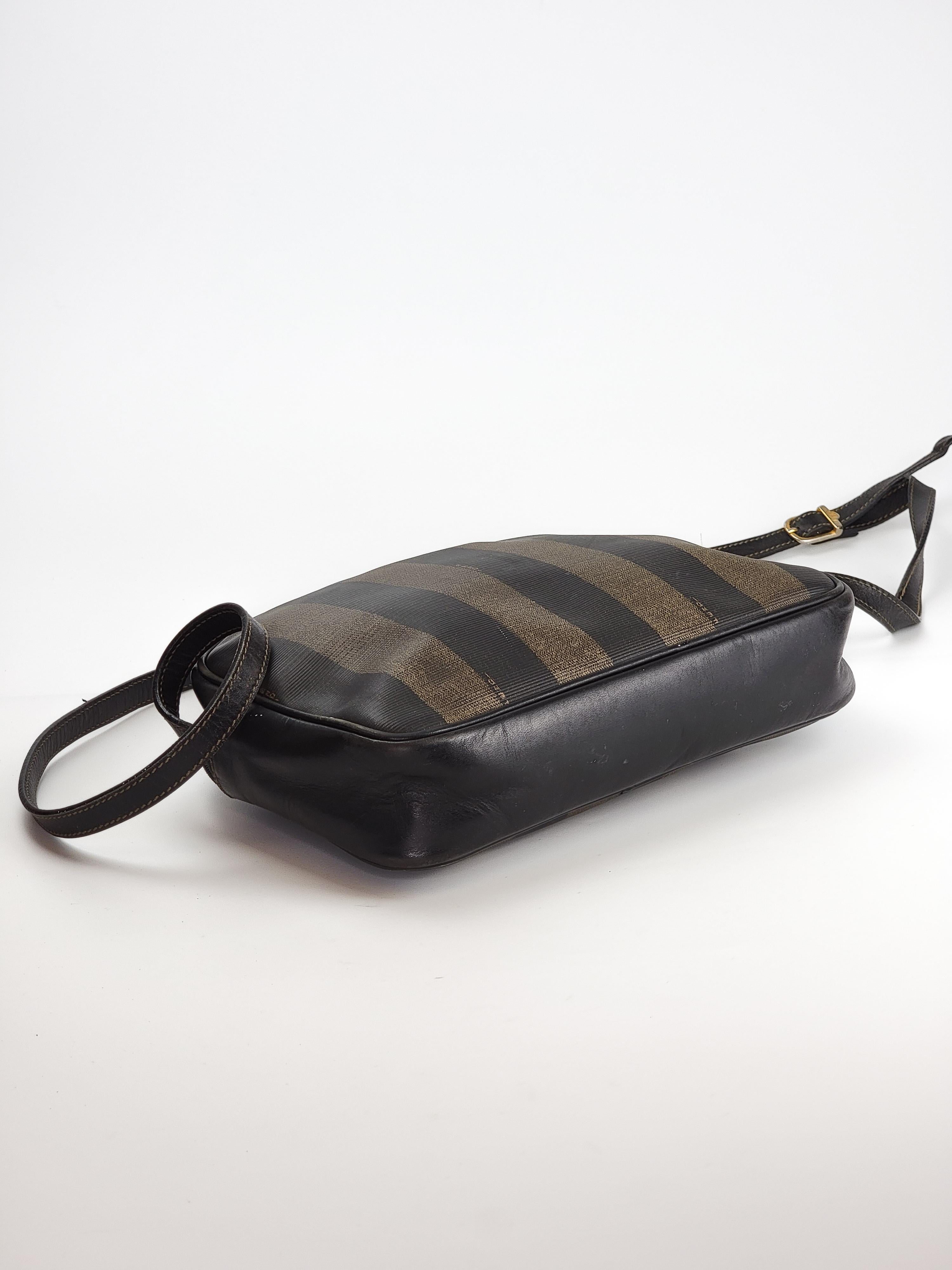 This vintage Fendi Pequin striped camera bag is made of brown and black coated canvas with an adjustable shoulder strap made of genuine black leather. This bag features an external pocket with the embossed Fendi logo on the front, which is also