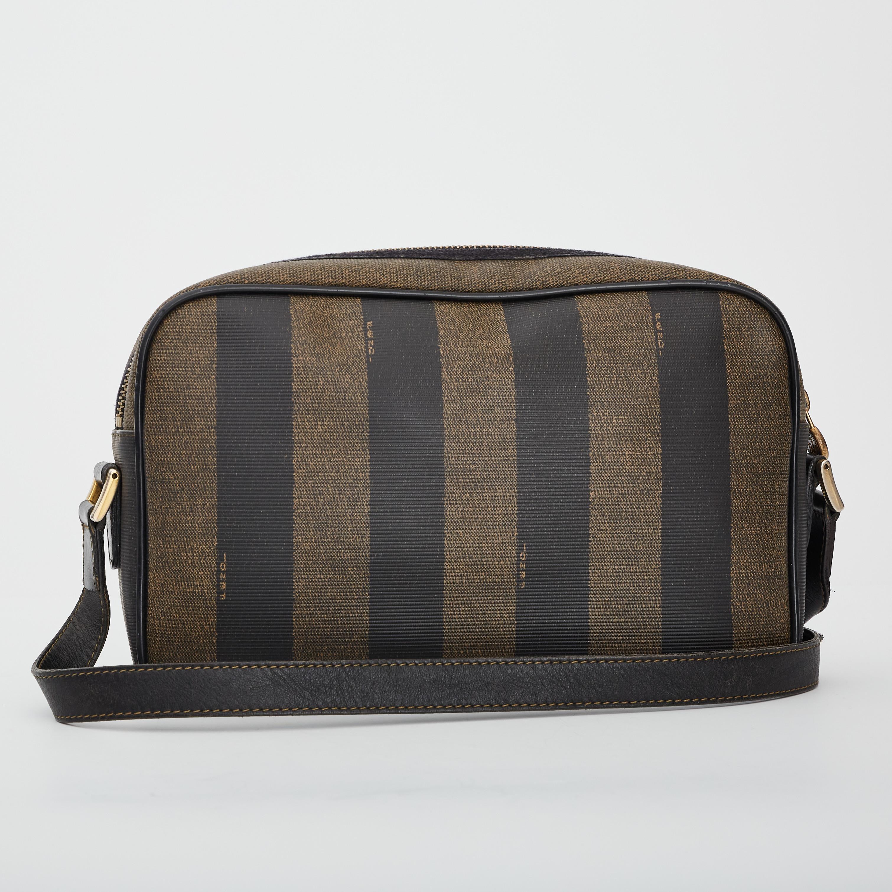 This vintage Fendi Pequin striped camera bag is made of brown and black coated canvas with an adjustable shoulder strap made of genuine black leather. This bag features an external pocket with the embossed Fendi logo on the front, which is also