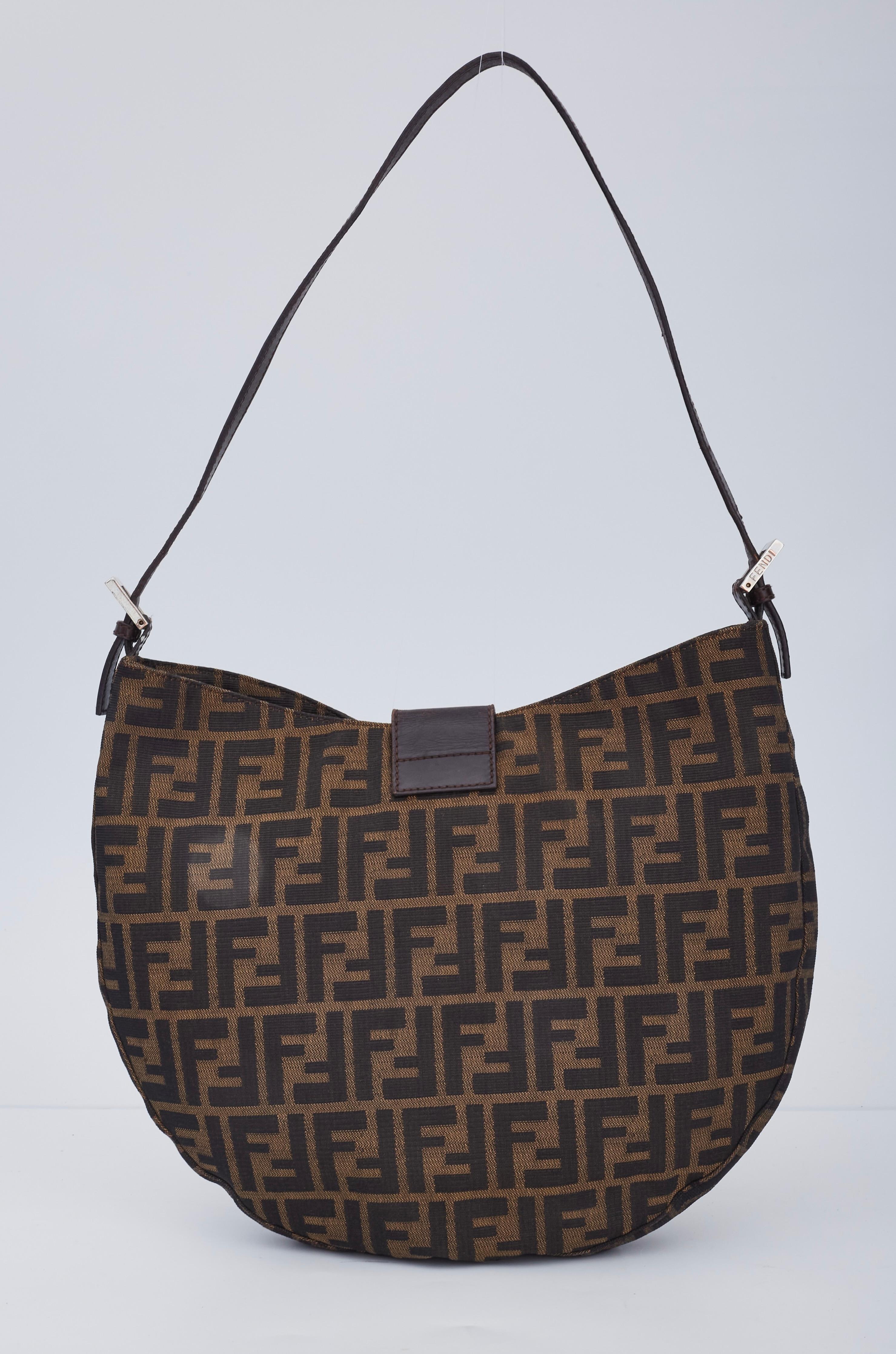This vintage crescent shaped bag is made with zucca logo fabric and features a flat leather shoulder strap, an open top, a leather strap flap at top secured with snap for closure and brown fabric interior with a patch pocket.

COLOR: Fendi monogram