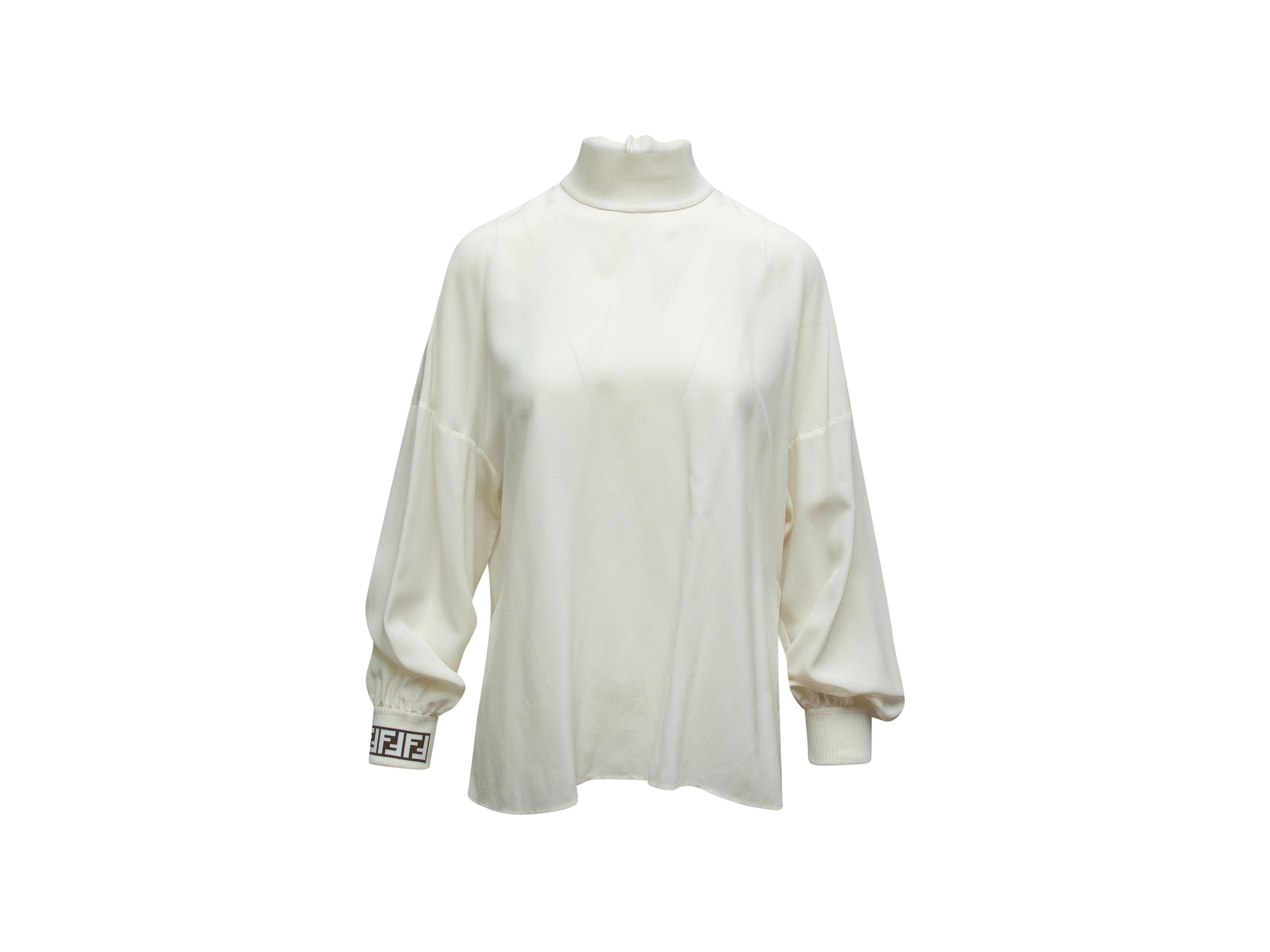 Product details: White silk long sleeve top by Fendi. Mock neck. Black logo print at cuff. Keyhole at back featuring button closure. Designer size 42. 38