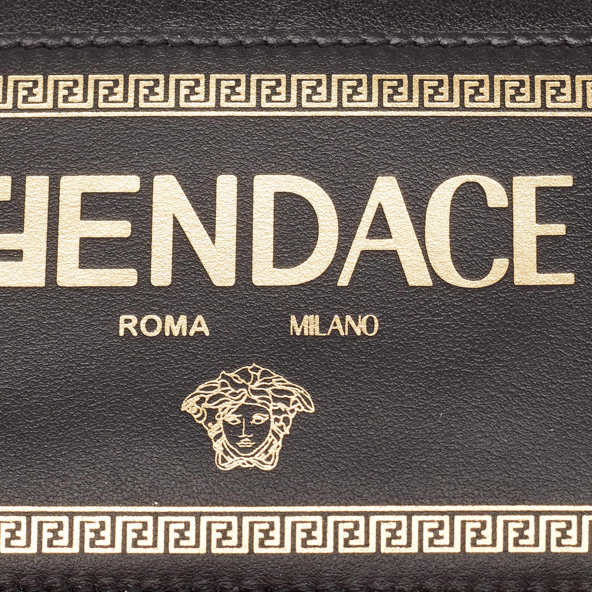 The Fendi x Versace Fendace card holder is a luxurious accessory featuring a sleek black leather exterior adorned with gold accents. The iconic Fendace logo adds a touch of opulence, while the lanyard provides practicality for holding cards. This