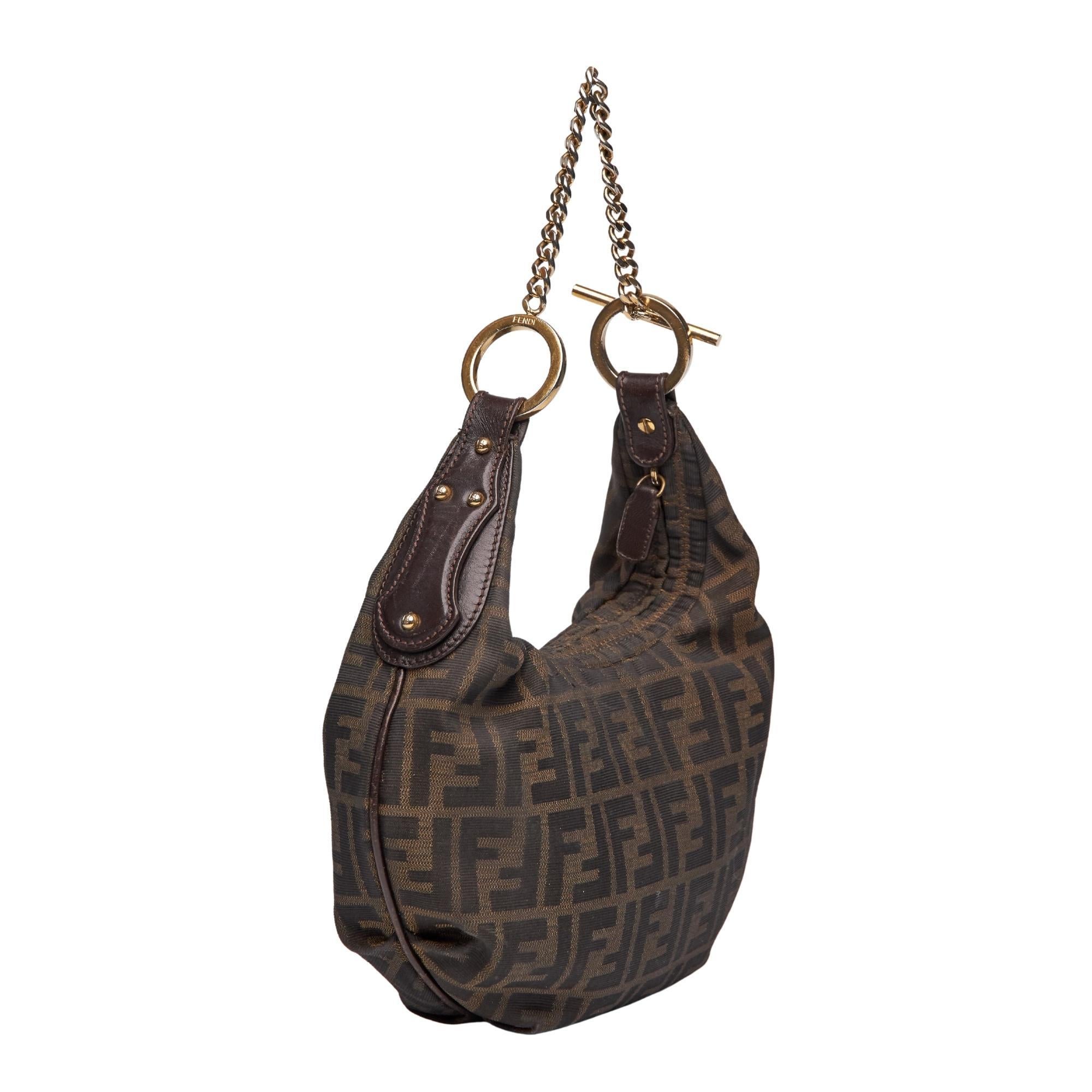 This Chef Chain Hobo bag by Fendi is a classic handbag with luxurious finishes. Made from zucca printed canvas with brown leather trim, this hobo is accented with a large gold Fendi engraved charm and gold chain link shoulder strap. The spacious