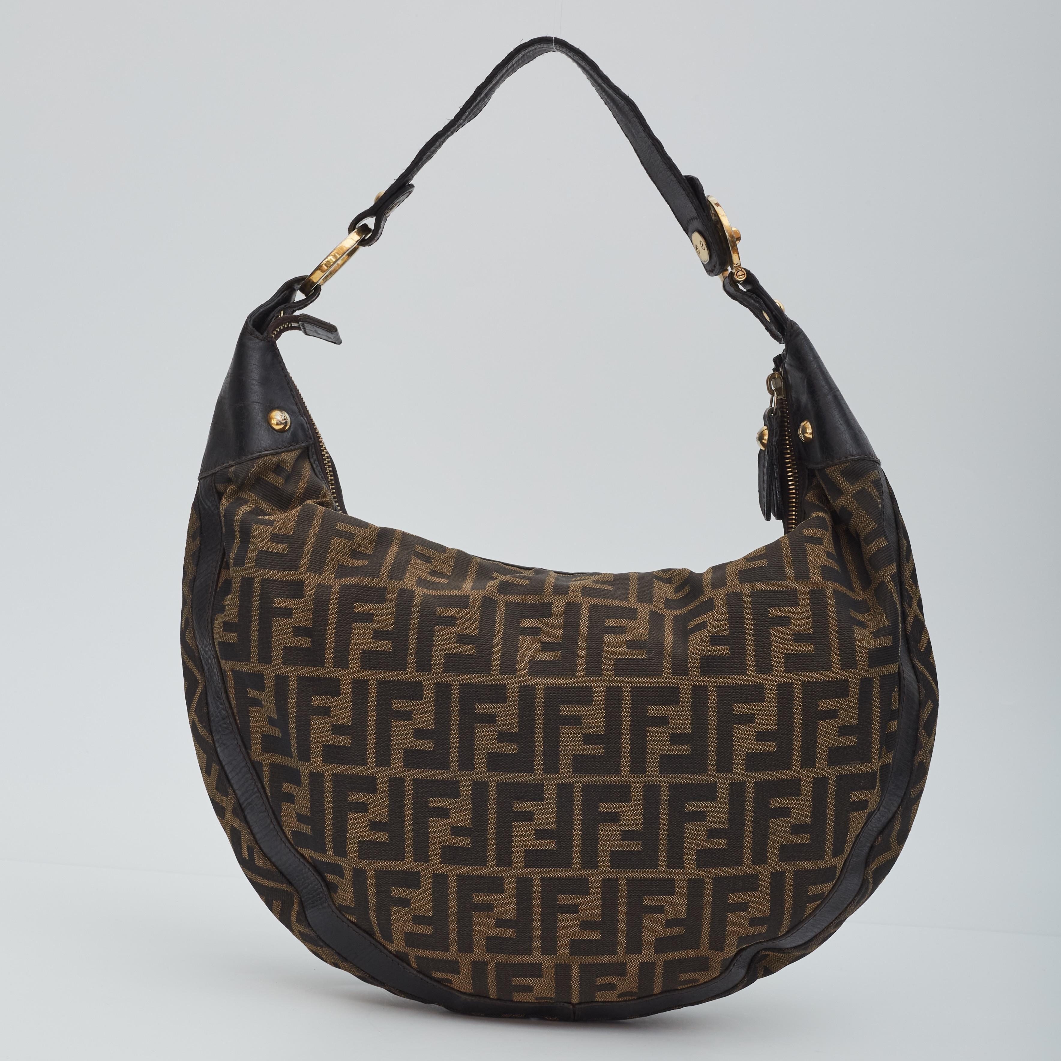 This hobo is constructed of Zucca print Fendi FF canvas with a croissant shape. The bag features leather trim and matching strap handle with gold links and studs. The top zipper opens to a cocoa brown fabric interior with patch pockets.

Color: