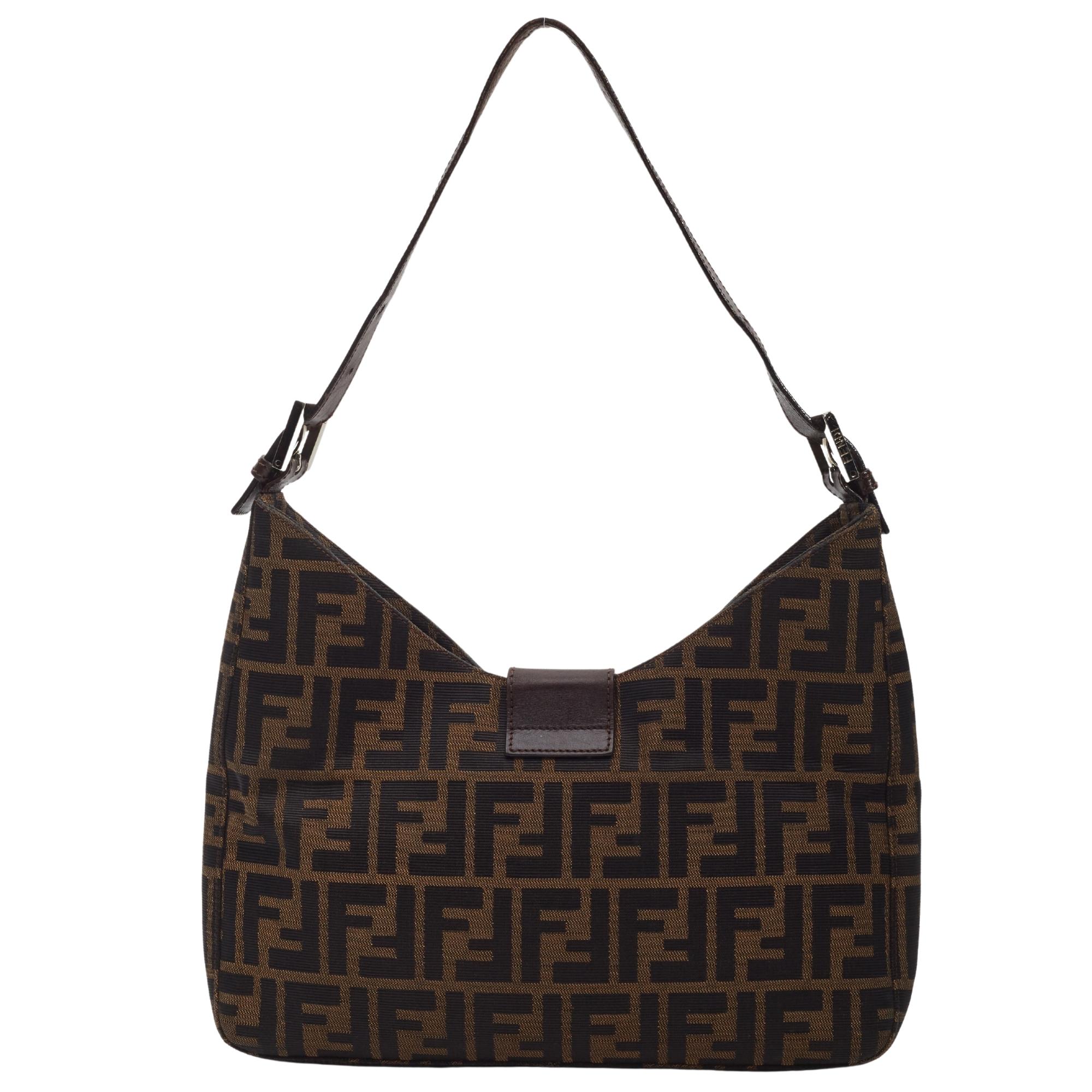 This shoulder bag is made of Fendi Zucca canvas in tobacco brown. The bag features an adjustable brown leather shoulder strap and a crossover strap with a polished silver Fendi FF logo. The flap opens to a brown fabric interior with a zipper