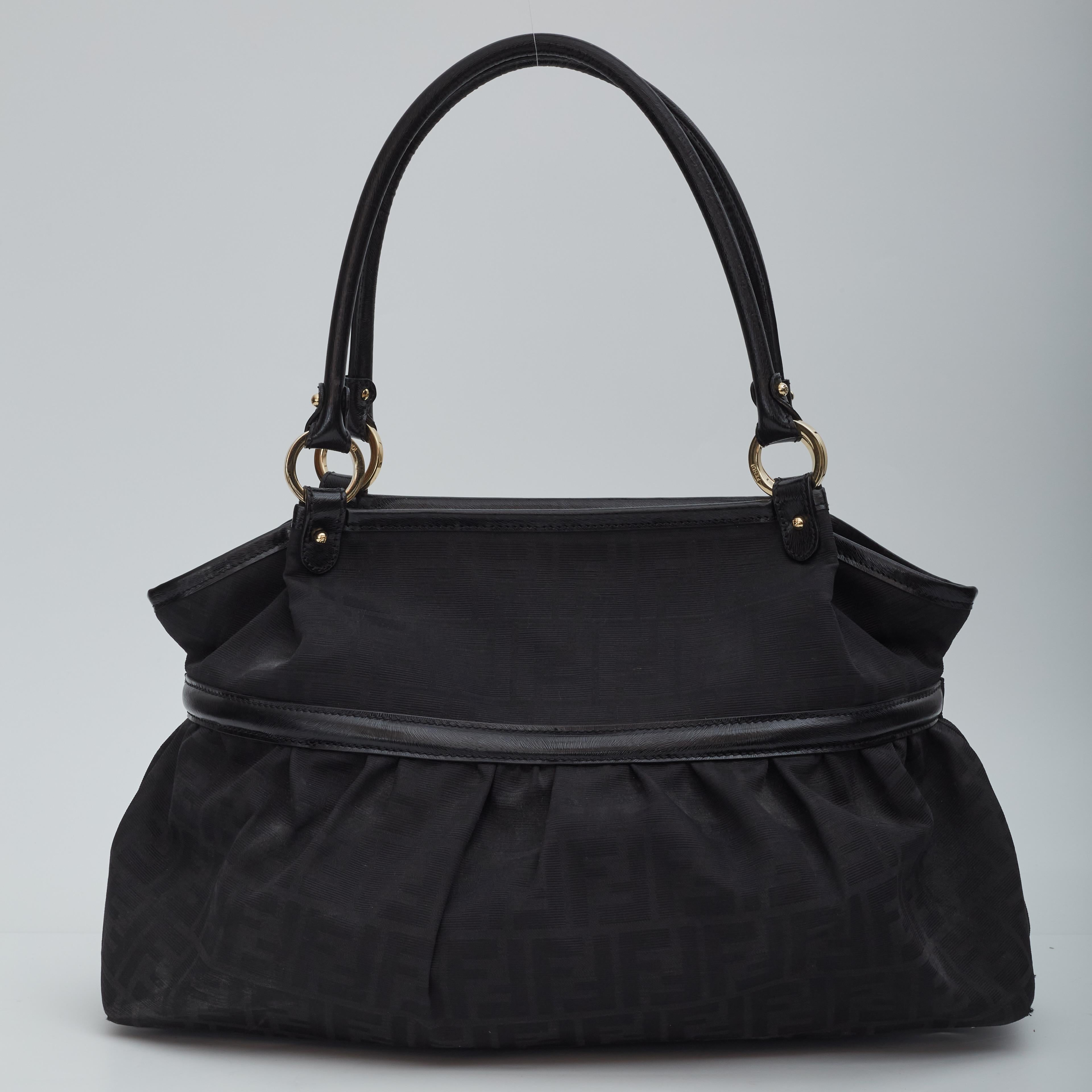 This bags constructed of signature FF Zucca canvas with black leather top handles and trim. The large disc-shaped Fendi handbag has polished brass hardware including handle rings and studs. The top unzips to a black fabric interior with a zip