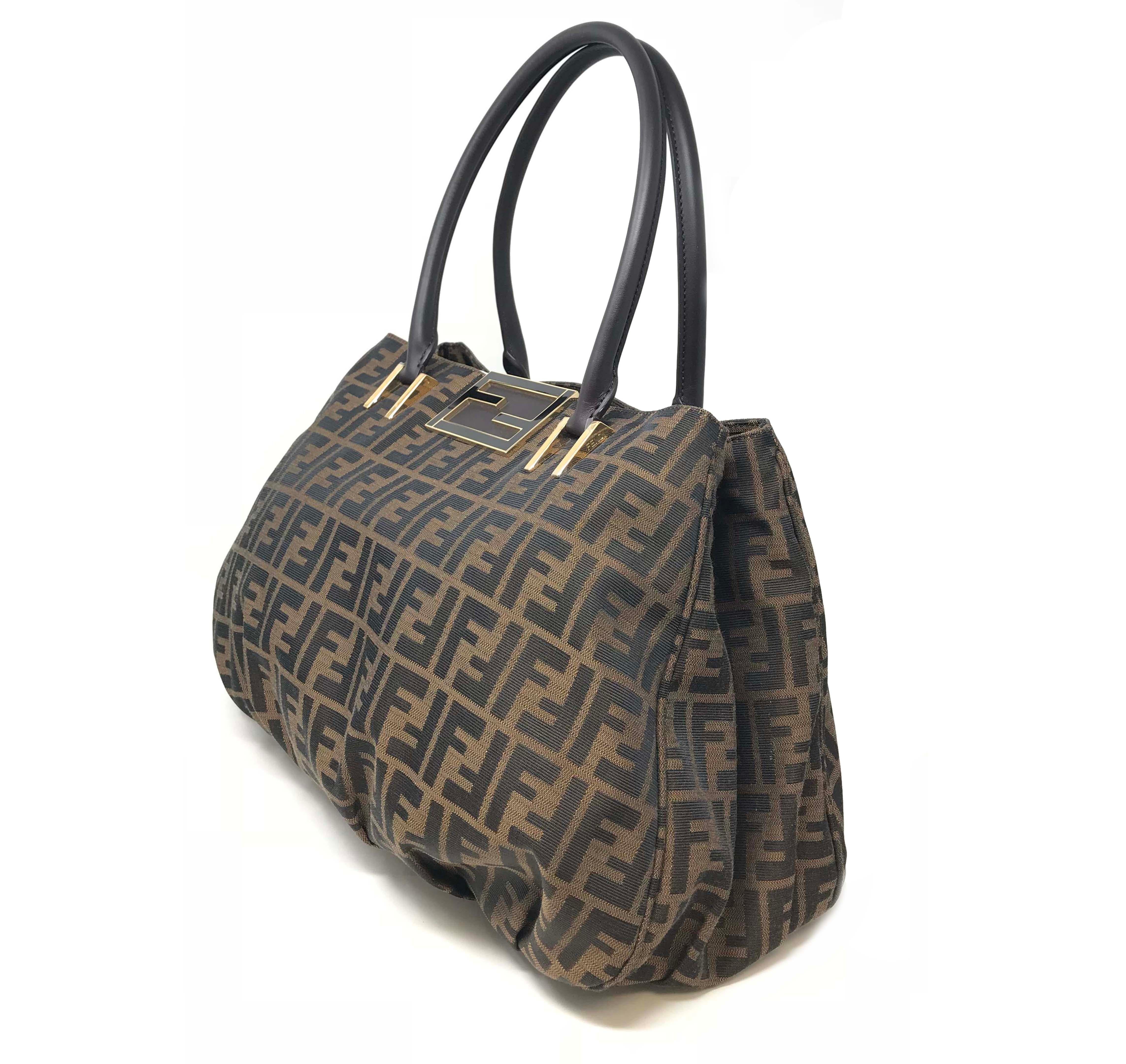 We guarantee this is an authentic FENDI Zucca Mia Tote Tobacco or 100% of your money back. This stylish tote is crafted of traditional Fendi FF Zucca tonal brown canvas. The bag features gold chain black patent leather threaded top handles as well