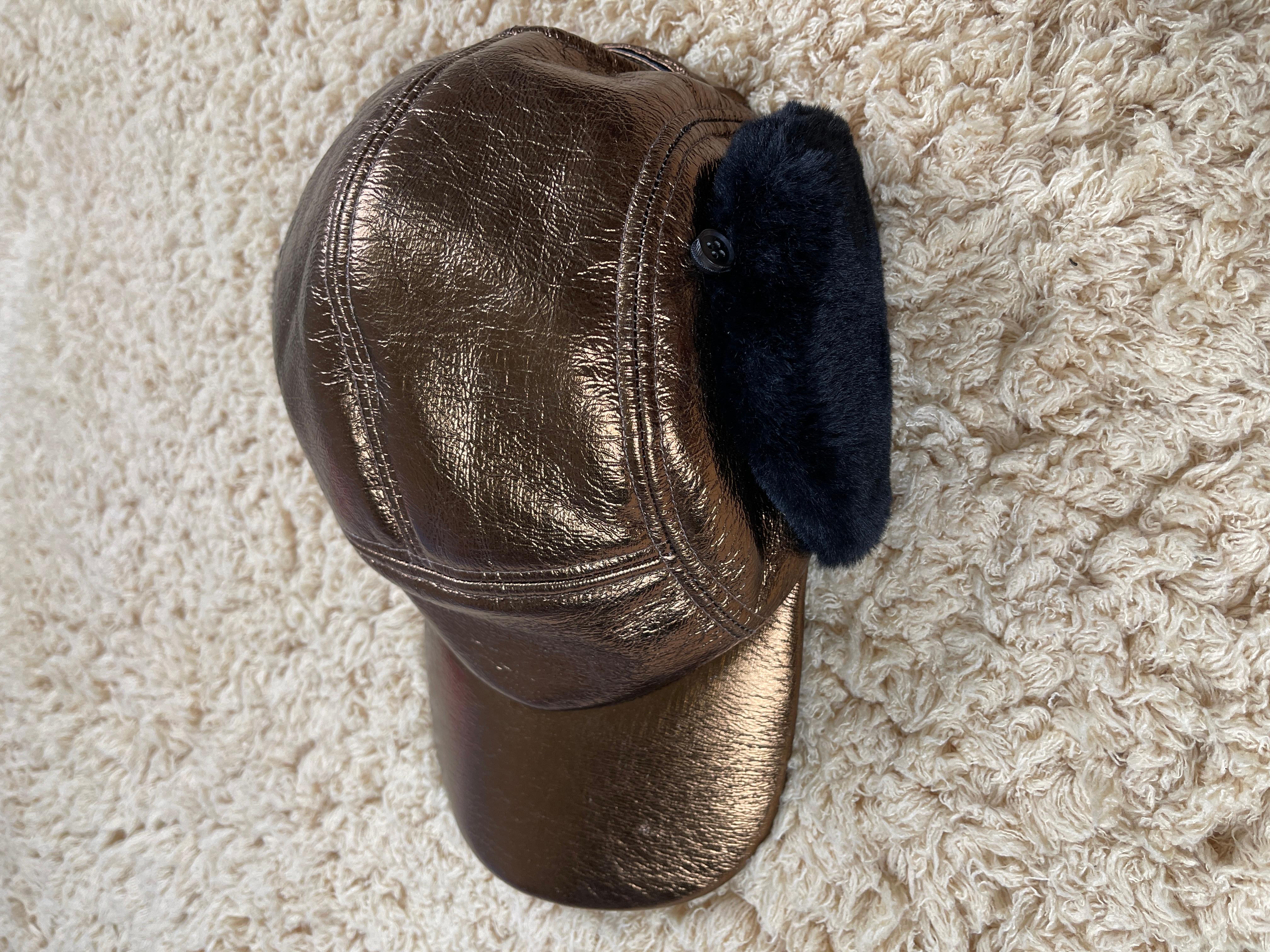 Lined with black faux-fur for the ear flaps, Feng Chen Wang demonstrates how she effortlessly has incorporated textures into this collection through the worn vintage feel of this cap. Coated in an almost metallic copper coating and finished with a