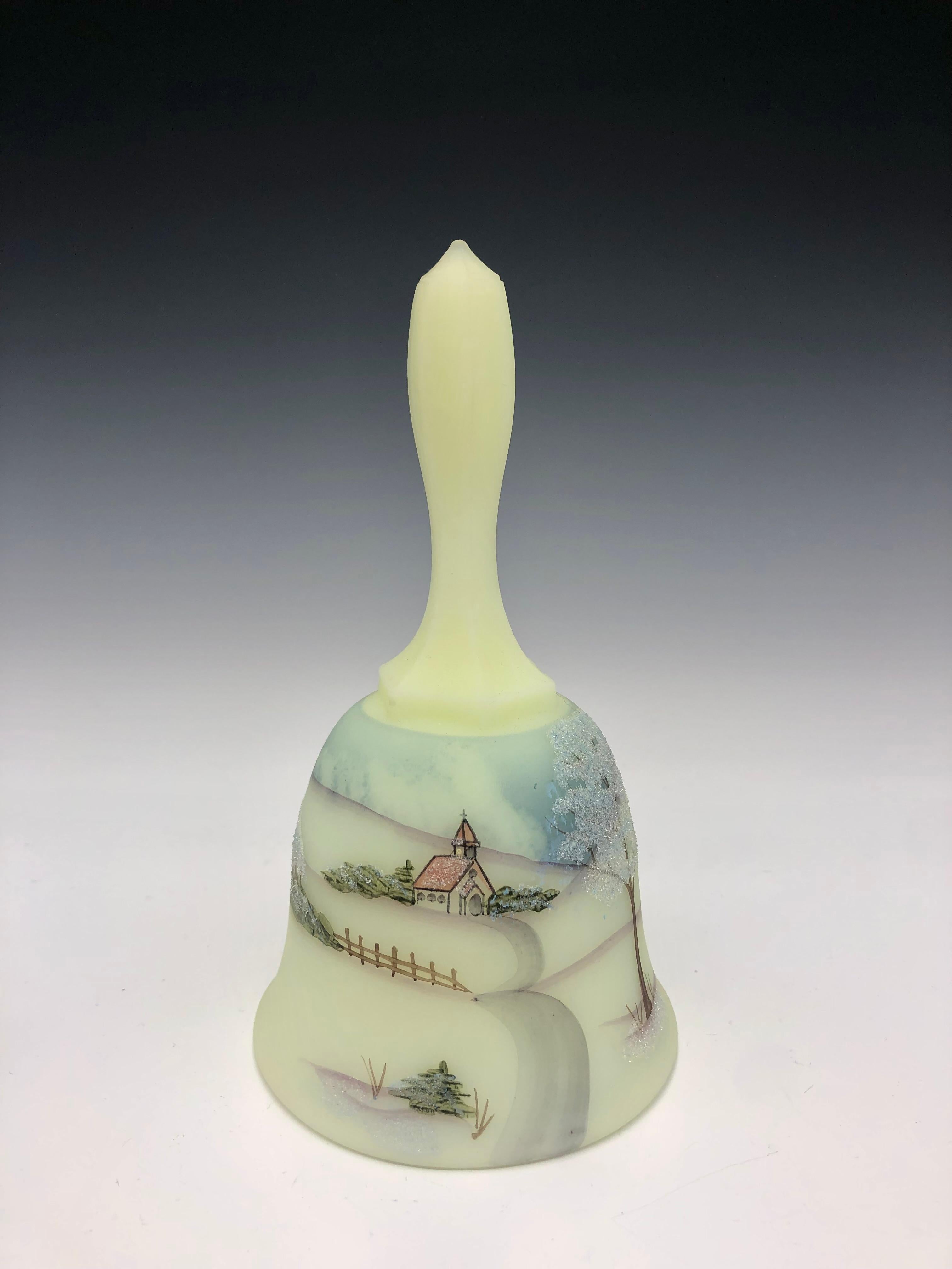 Pale green/yellow Fenton vaseline custard glass bell adorned with delicately painted winter country church scene. 

The bell is hand-painted and signed on the interior by artist S. Meunier; a charming, beautifully crafted item made in 1980 as part
