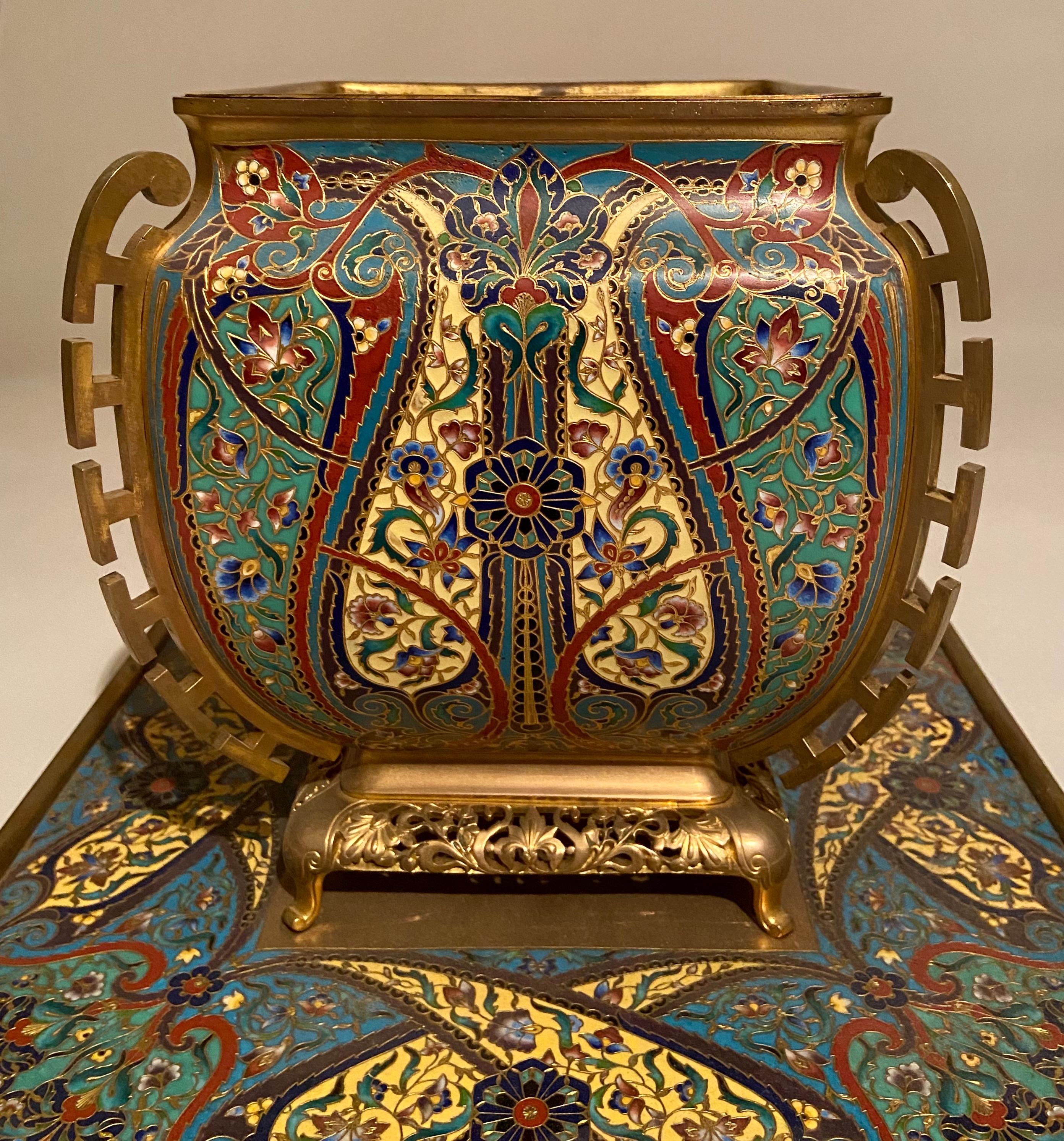 Shaped square, the stand on four bun feet, the vase with detachable liner, champlevé enamel and gilded bronze. Circa 1870. The base signed F. Barbedienne.