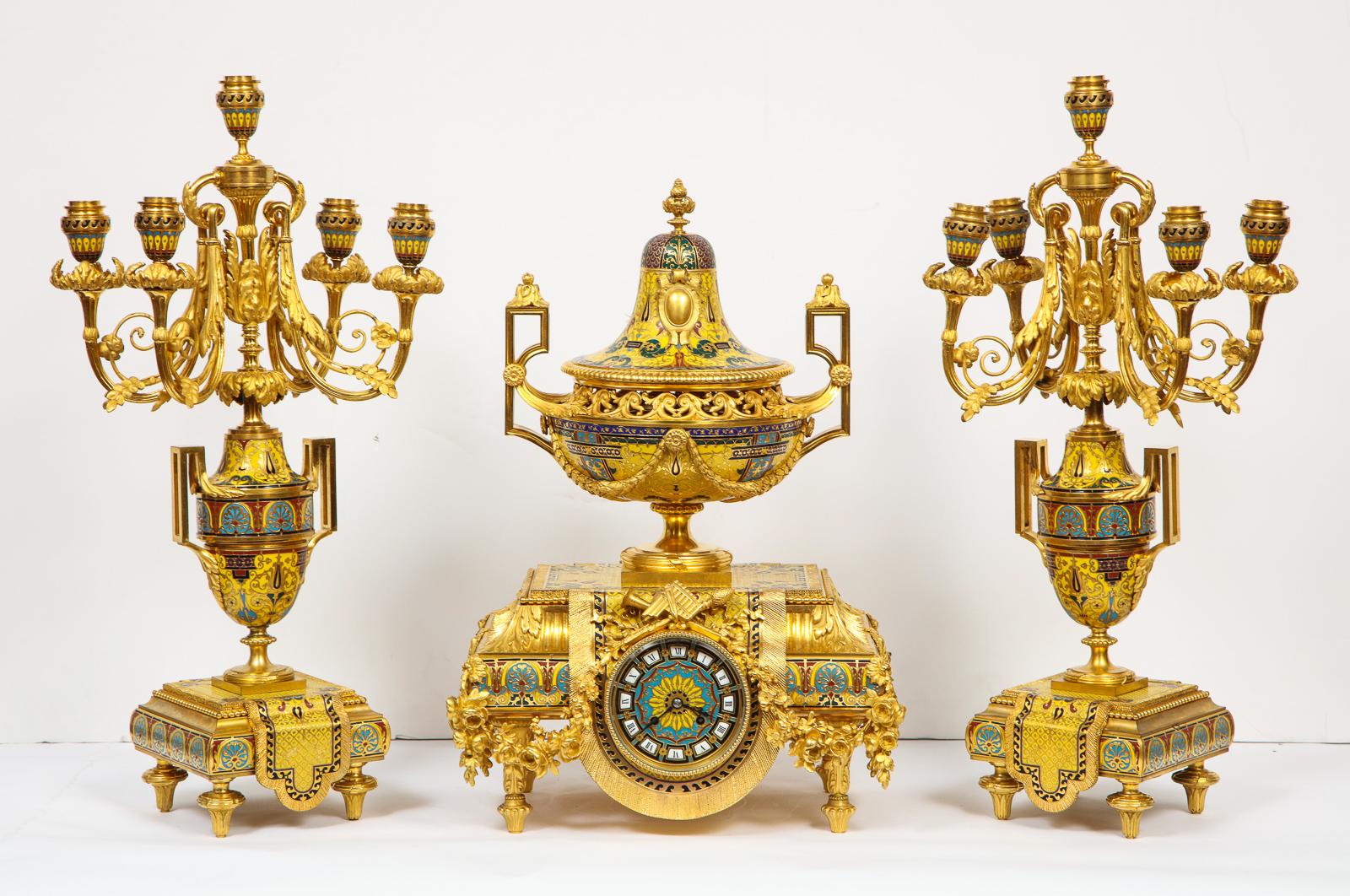 Ferdinand Barbedienne, A Museum Quality French Ormolu Champleve Enamel three-piece Clock Set Garniture.

Comprising of a clock and a pair of Candelabra, with the highest quality French ormolu or bronze and champleve cloisonne enamel.

The clock in