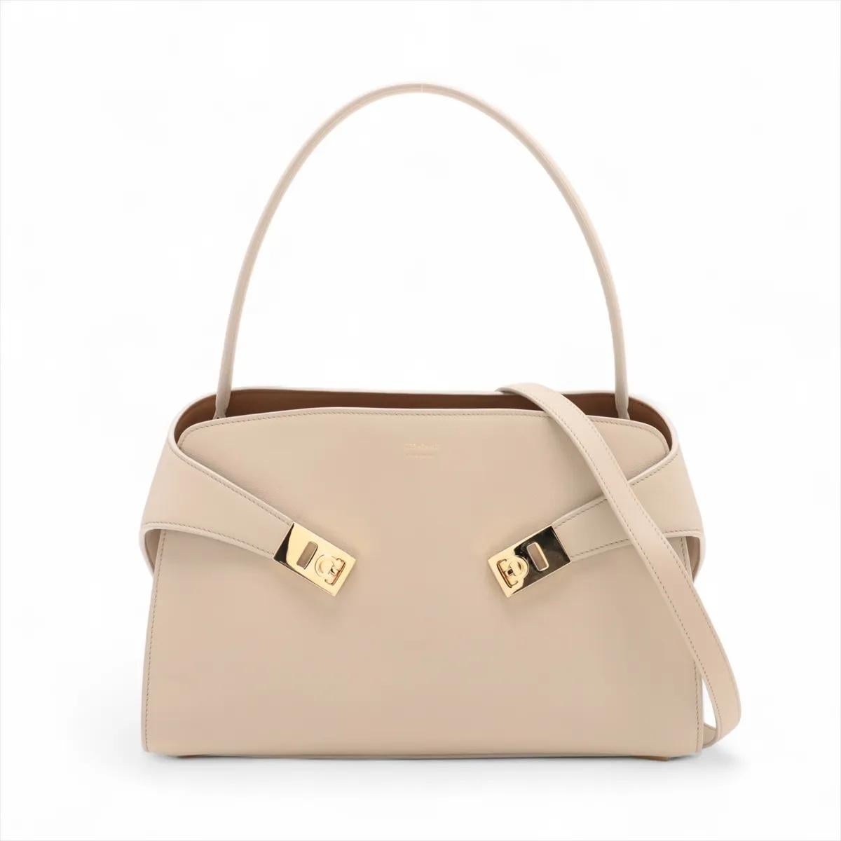 La borsa Ferragamo Hug in pelle beige è un accessorio raffinato ed elegante che mette in mostra l'impegno del marchio verso un'artigianalità senza tempo e un design moderno. Realizzata in pelle liscia e di alta qualità, la borsa presenta linee