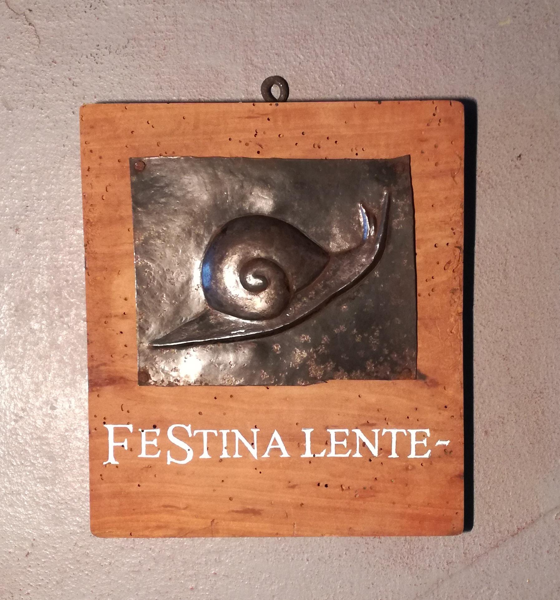 Festina Lente, antique hostaria sign. heavy metal plate with relief figure, mounted on solid wood panel. many woodworm marks are present. woodworm treatment has been done. writing is more recent.
Festìna lente 