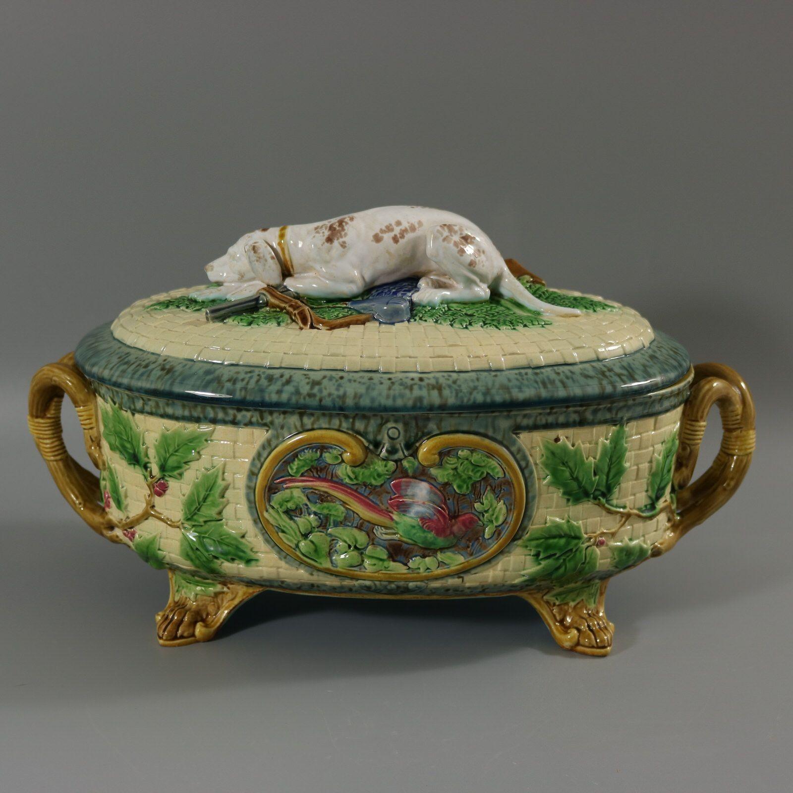 Minton Majolica game pie dish with liner which features a hunting dog asleep next to a gun, a powder flask and a game bag. Colouration: cream, green, brown, are predominant. The piece bears maker's marks for the Minton pottery. Bears a pattern