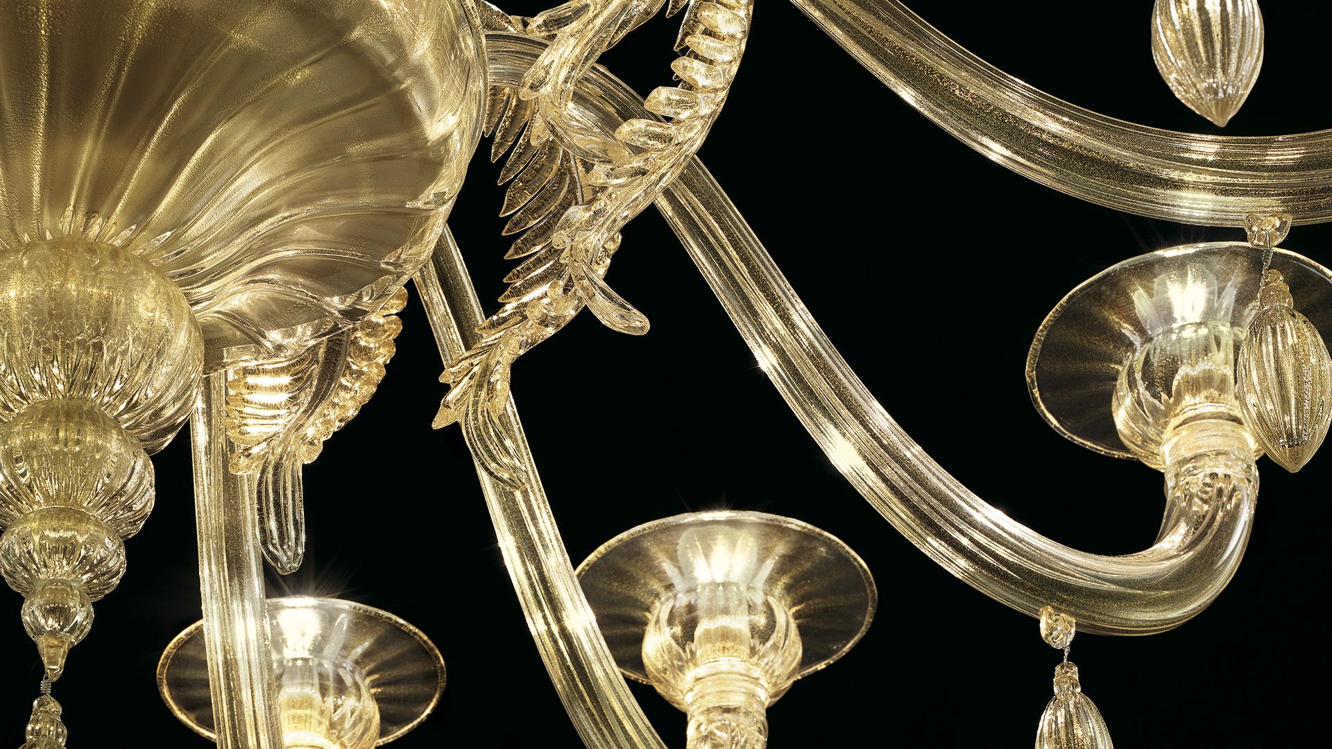 Le lustre Fez 5602 12 a été initialement conçu en 2011, et est présenté ici en verre soufflé Gilded Gold, et en finition Galvanized Gold. Les feuilles dorées et les pendentifs en forme d'olive sont à l'honneur dans cette collection de lustres et