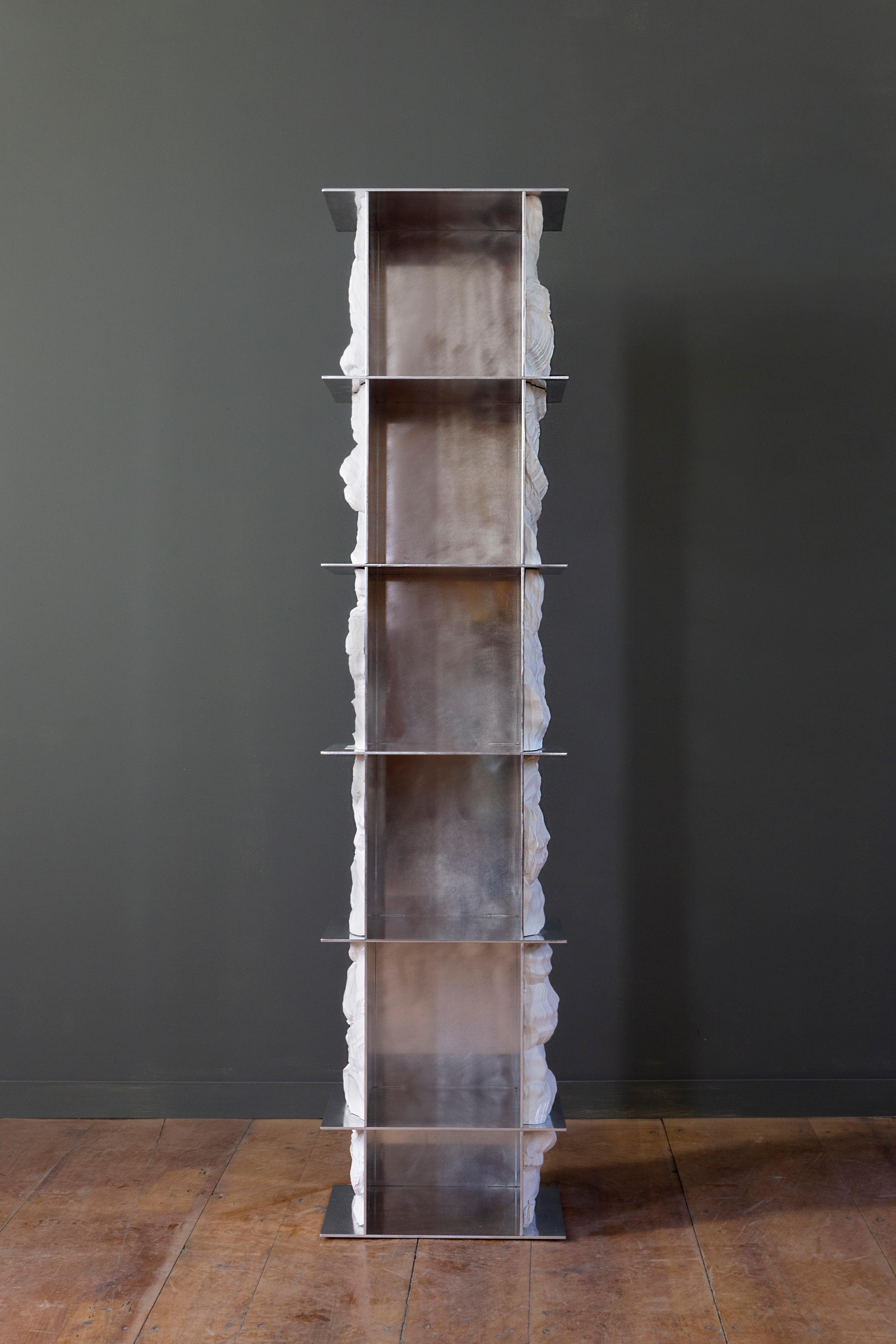 A slender tower-like sculptural bookcase, made from a rigid hand polished aluminum structure. Through the grid-like structure, a cast form of the collection's signature texture flows continuously through the layers. The polishing of the aluminum