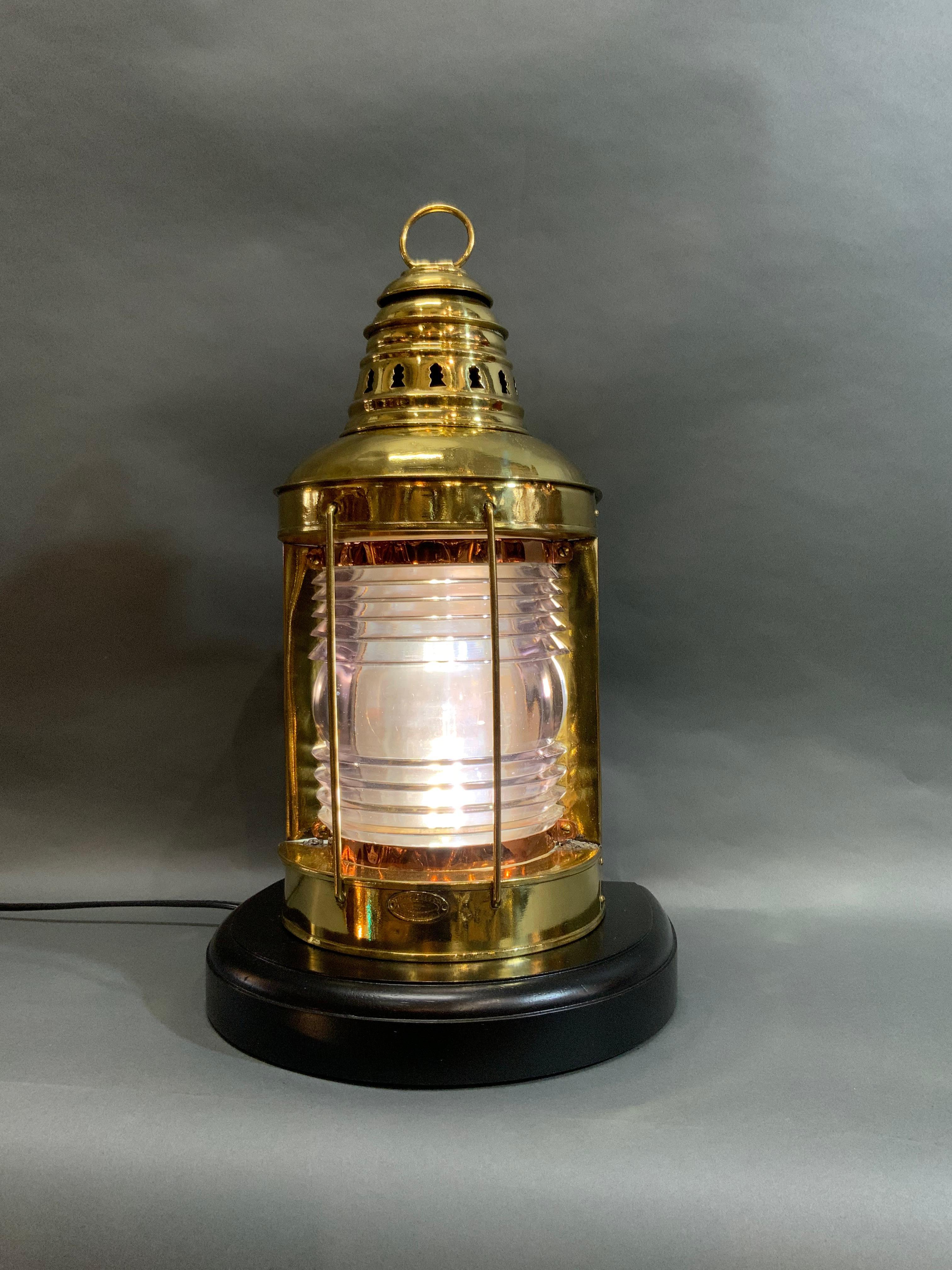 Maritime lantern by F.H. Lovell of solid brass with protective brass bars and glass Fresnel lens. Vented top and original hoisting ring. Mounting bracket to backside. Great nautical lantern that has been wired with socket for home use and mounted to
