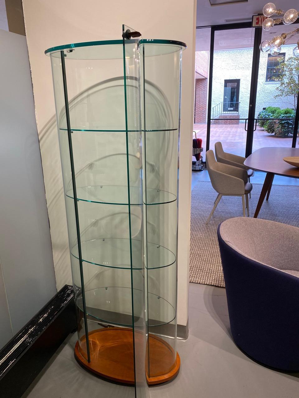 SHOWCASE IN CURVED GLASS
Wired showcase in 6 mm-thick curved glass, with four 6 mm-thick glass shelves (L 58 cm, W 31 cm), 12 mm thick glass top, door with lock. Profiles in brushed aluminium glossy finish. 
canaletto walnut wood base.