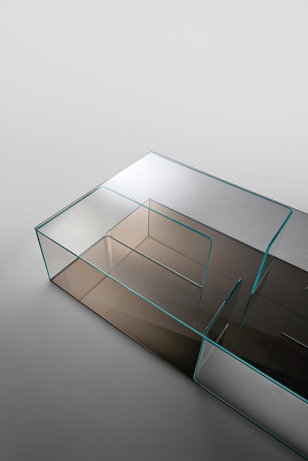 Coffee table/storage unit composed of 4 elements in 10 mm curved glass mounted between two 10 mm glass racks. Top and partitions in extra light glass, bases available in extra light glass, back-painted extra light glass, extra light mirrored glass,