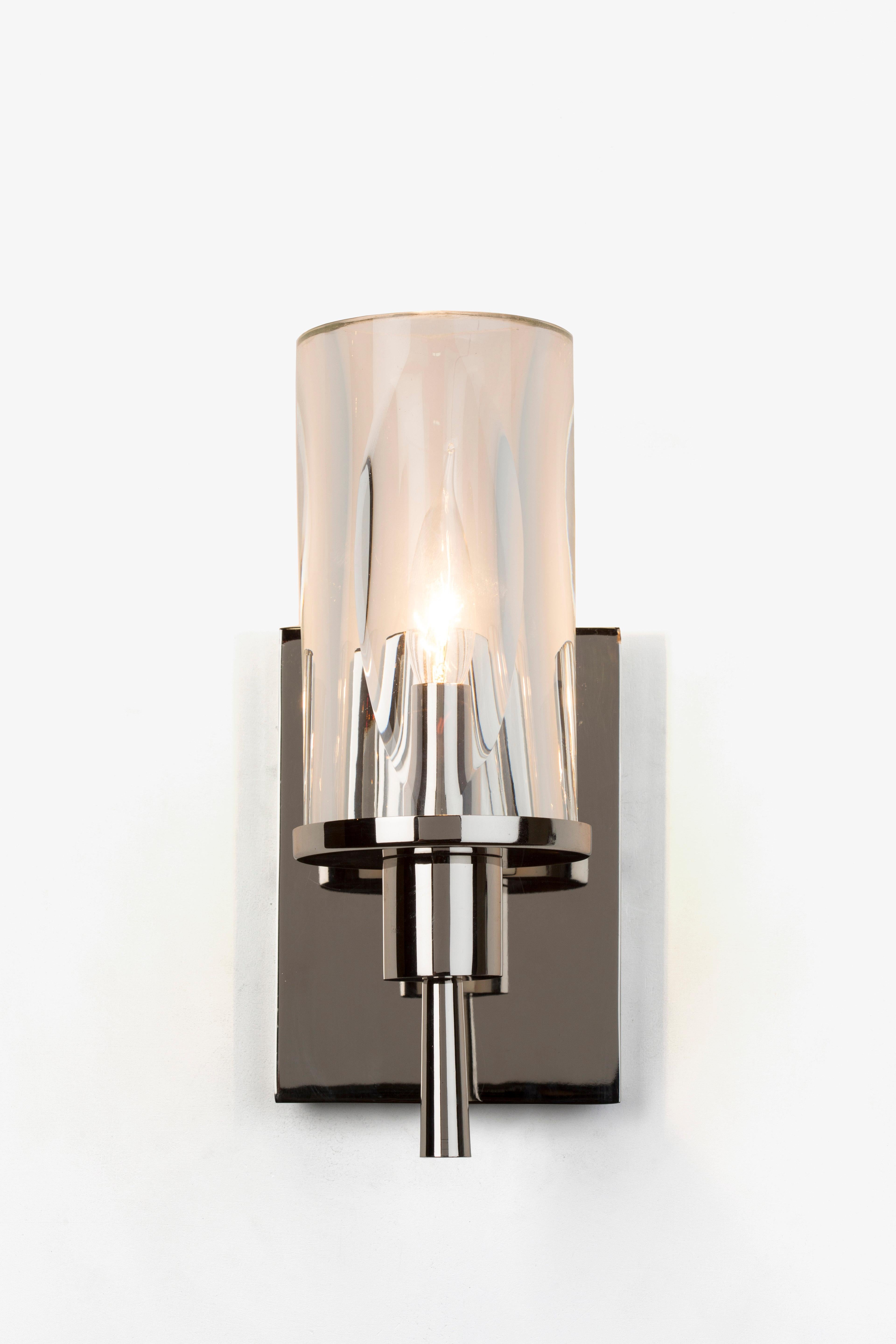 The FIAMMI wall sconce has Beautiful hand blown glass shades with unique ‘flame’ facets cast graceful shadows as they float on the elegant frame of luxurious metals with a contrasting wood detail. Graceful and refined, FIAMMI is a study in organic