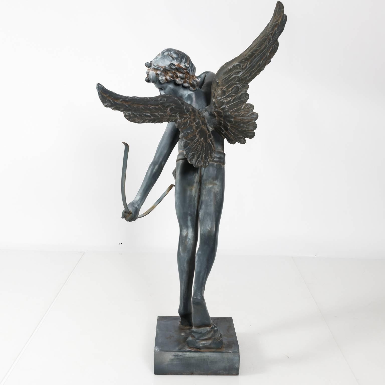 Contemporary fiberglass and iron garden cupid firing his bow and arrow at a target. This piece is in a weathered finish.
 