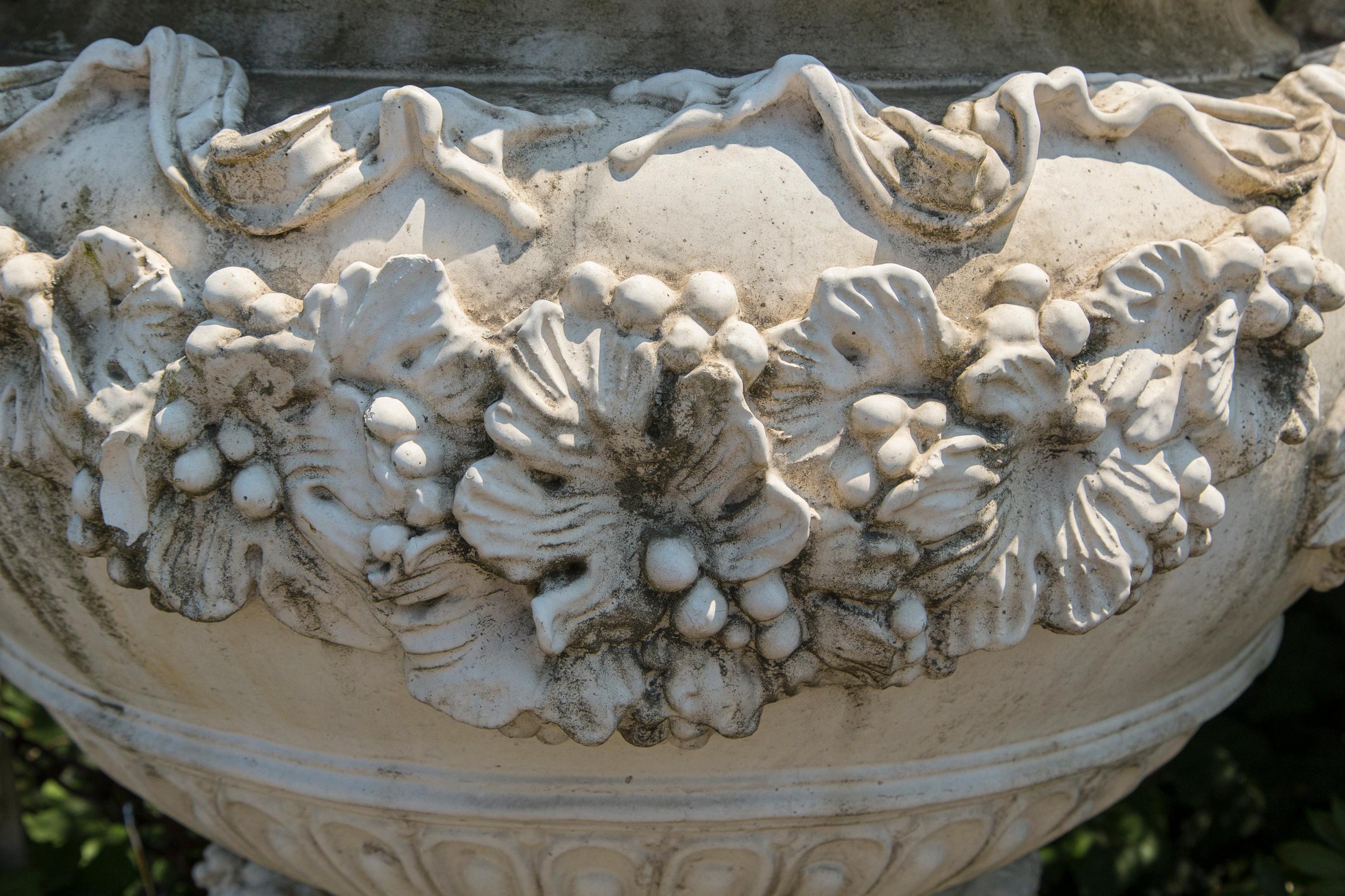Cast from the 18th century French original, base with 4 seated putti. Large basin flanked by handles. The basin edged with gardrooning, the body covered with grape leaves and bunches of grapes. The base measures 20 x 20. and the bowl has an opening