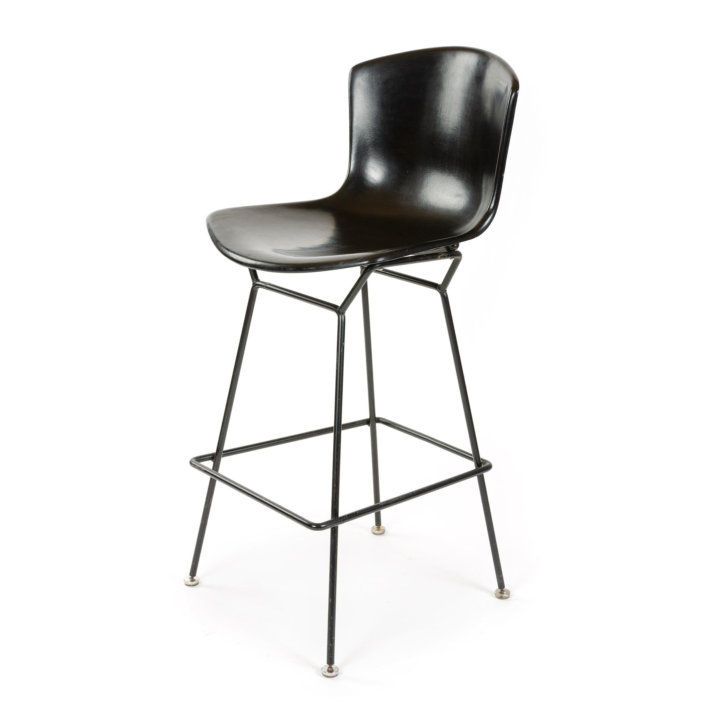 A barstool with a black fiberglass shell on splayed, painted legs.