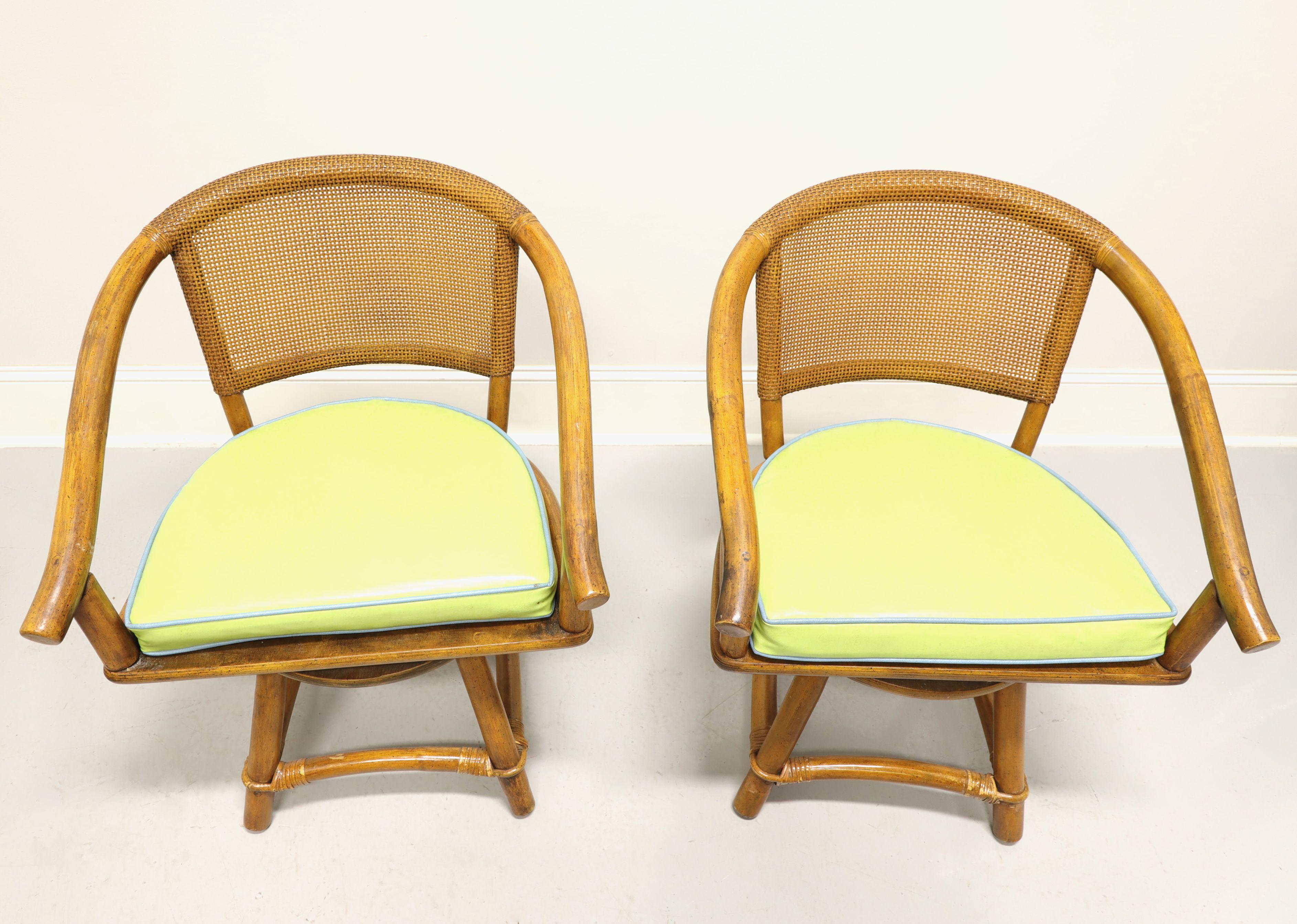 A pair of mid-20th century Coastal style swivel seat armchairs by Ficks Reed. Faux bamboo frame, cane backrest, rattan strapping, downward sloping curved arms, return-to-front swivel seat mechanism, plain wood seat meant to be used with a cushion,