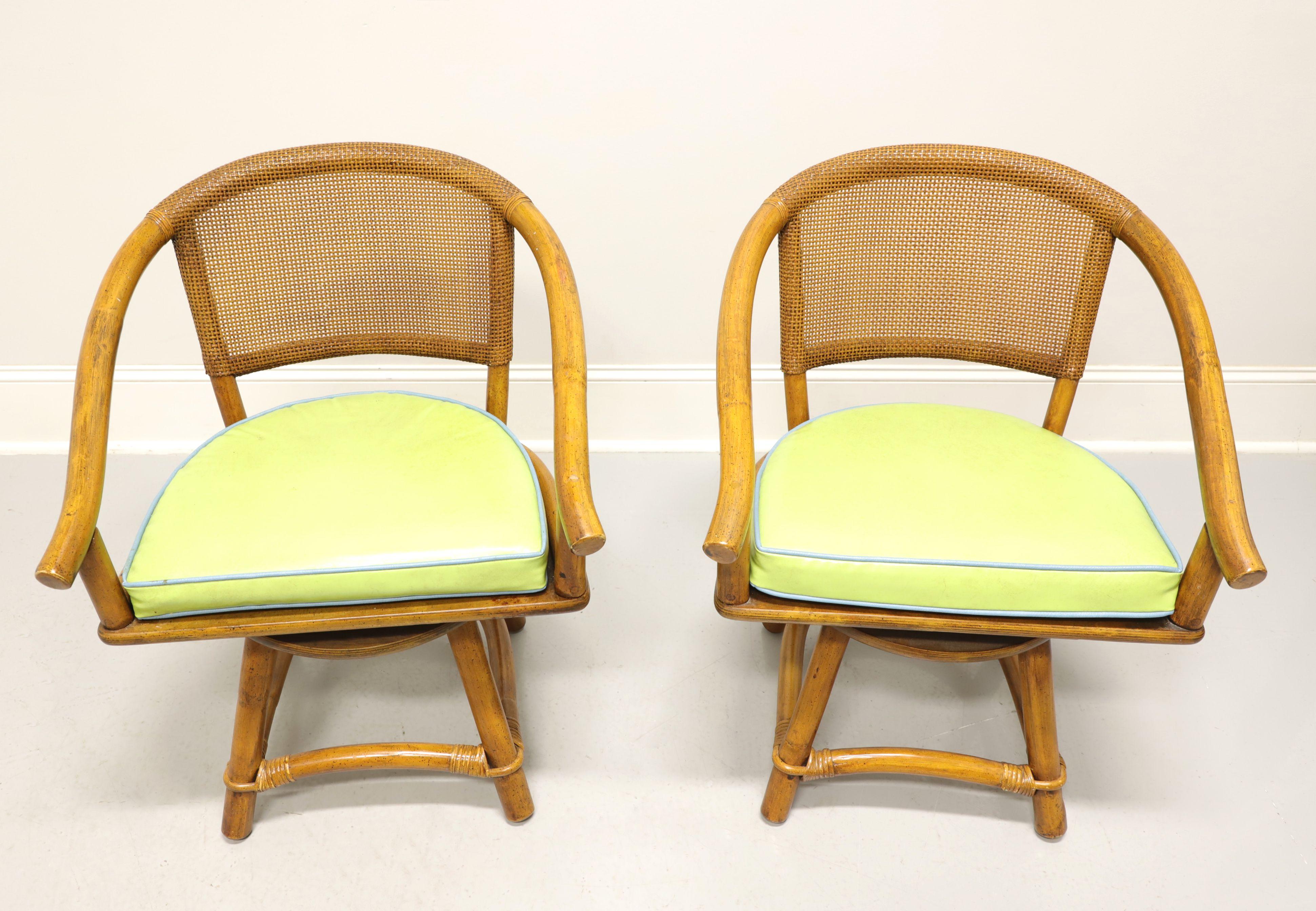 A pair of mid 20th century Coastal style swivel seat armchairs by Ficks Reed. Faux bamboo frame, cane backrest, rattan strapping, downward sloping curved arms, return-to-front swivel seat mechanism, plain wood seat meant to be used with a cushion,