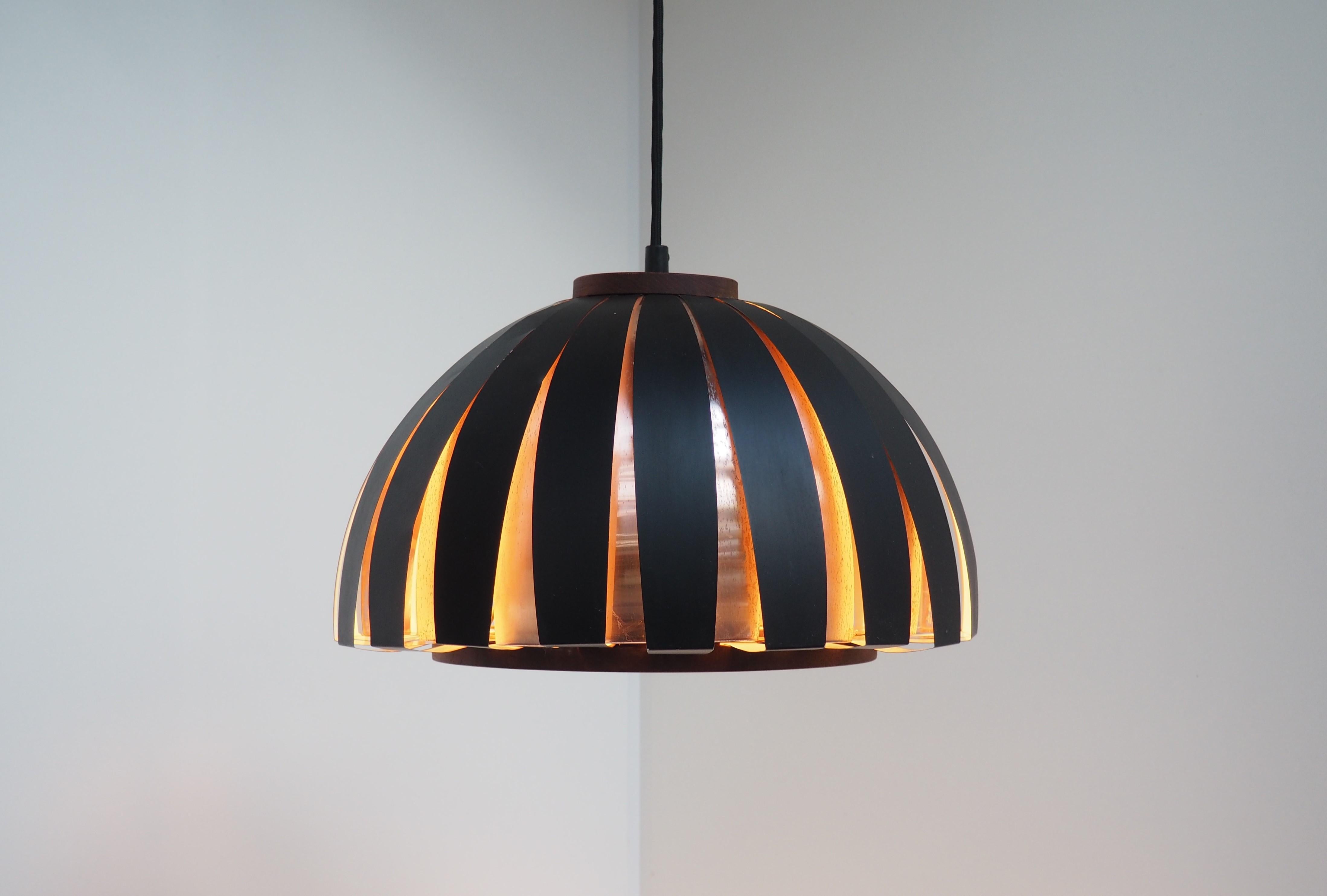 Fiesta pendant made by the Danish designer Svend Aage Holm Sørensen in the 1960s. The pendant is manufactured in solid copper and black painted metal slats and it has a thick decorative teak plate at the top and a teak wooden ring at the