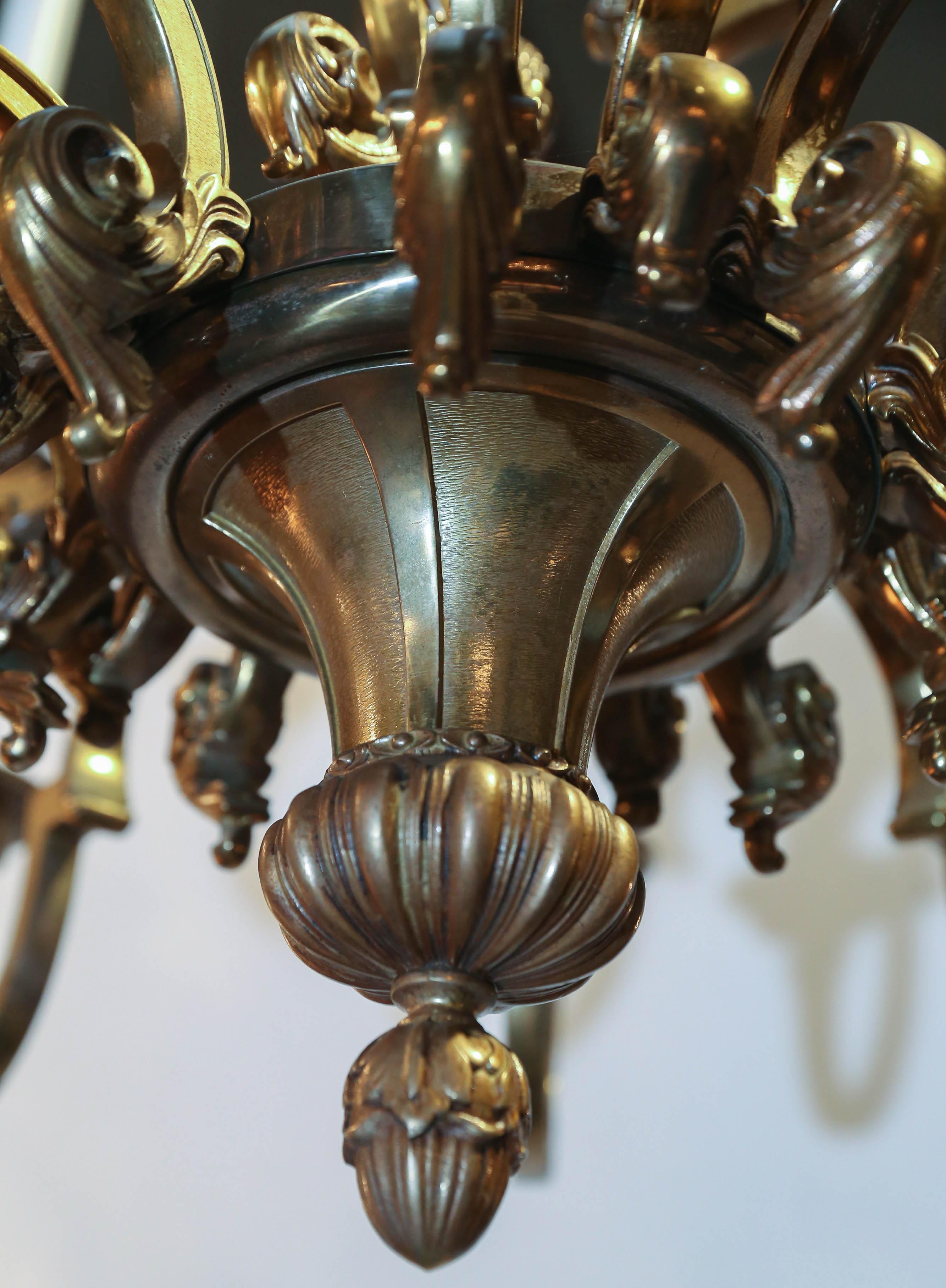 Fifteen-light two-tier neoclassical bronze chandelier has an antique gold finish.
Decorative details include two cherub heads, heavily detailed arms with acanthus designs.
Chandelier also features elaborate bobeche and candleholders, as well as an