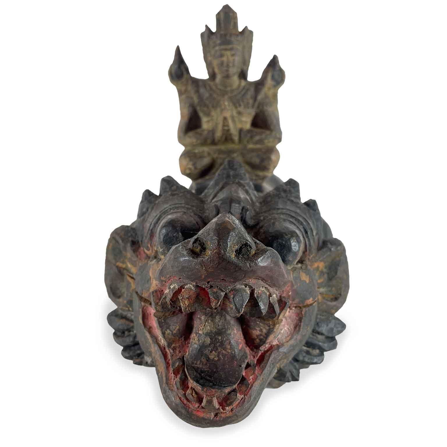 Escultura de animal fantástico con divinidad tallada a mano en una sola pieza maciza de madera exótica, probablemente teca,  con restos de policromía, representa la figura ficticia de un león, un león guardián tumbado con dientes y garras afilados, 
