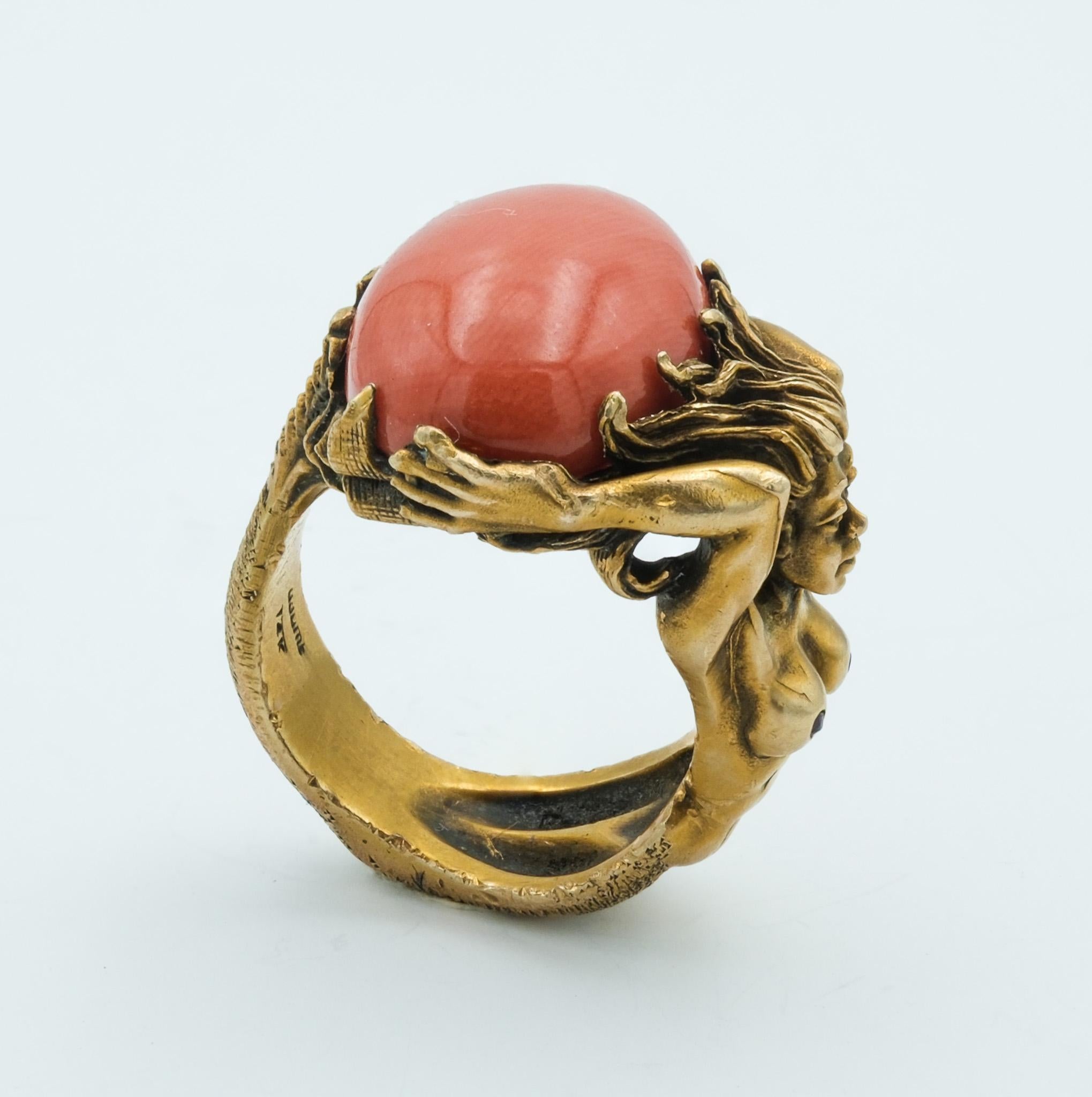 This exquisite piece is a unique ring that conjures the fluidity and grace of the natural world. Crafted from 14 karat yellow gold, it features a central coral gemstone, weighing approximately 12.8 carats. The coral's deep, warm hue is framed by a