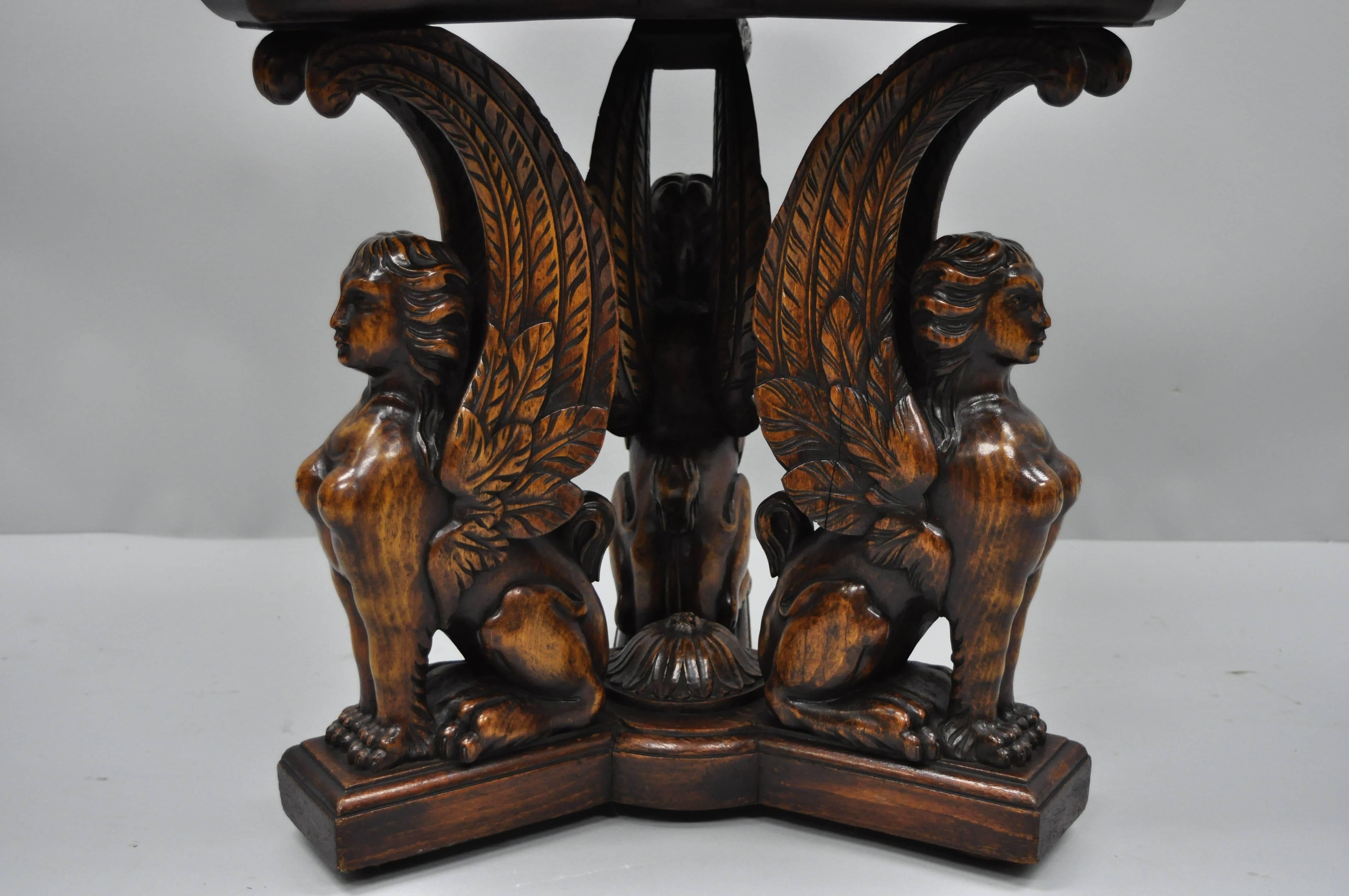 Figural carved walnut winged maiden griffin accent table. Item features solid carved walnut winged maiden griffin figures, triangular top with specimen and resin inlay, solid wood construction, very fine details, attractive style and form, early
