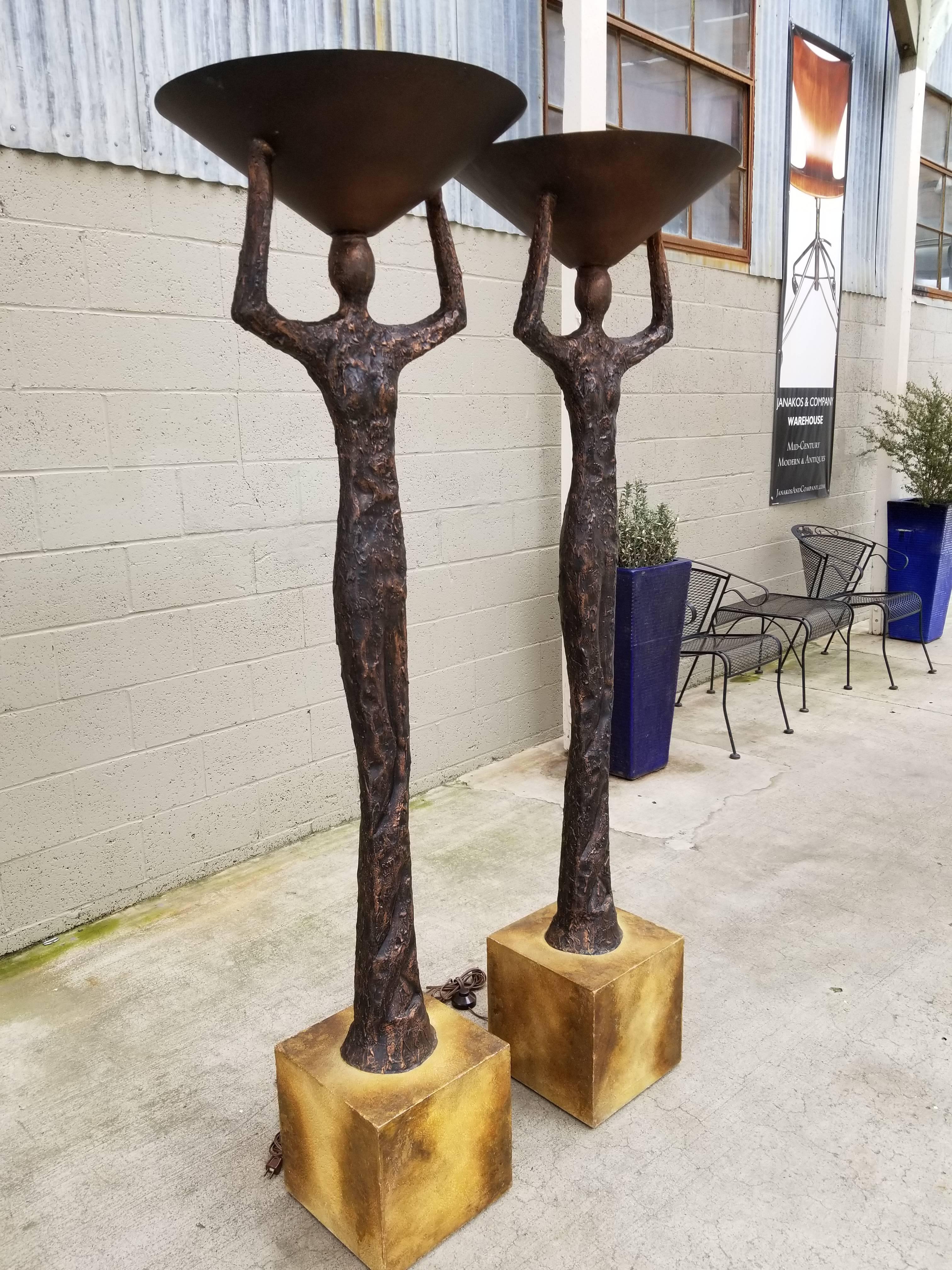 A pair of torchiere floor lamps in the manner of Alberto Giacometti. Heavily textured finish resembling patinated bronze. Wood bases with steel weights. Steel cone shades. Figures are a hallow fiberglass with applied resin for texture. Impressive
