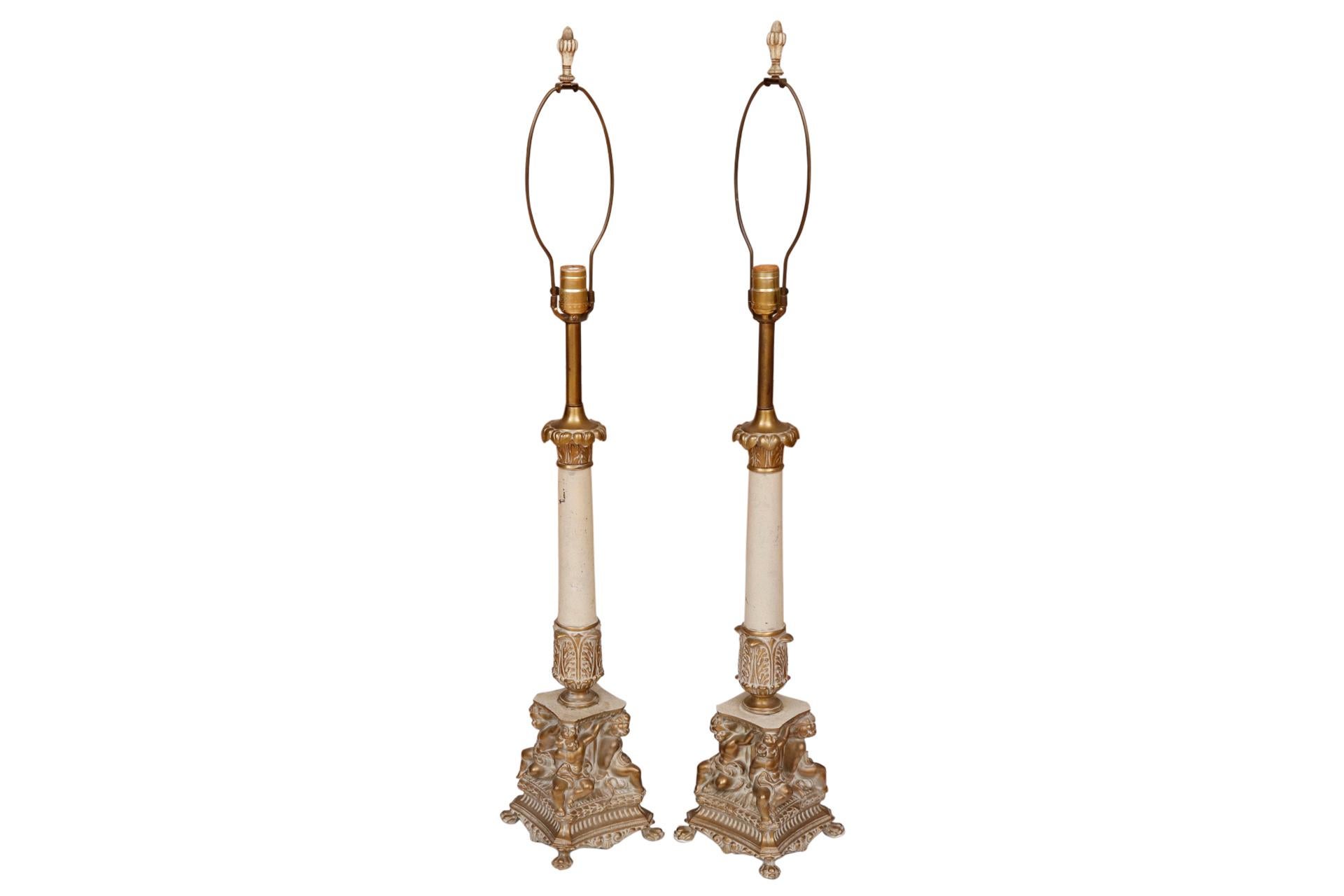 A pair of figural French Empire style table lamps. White metal columns are topped with cast acanthus plumes and finished with palms at the base. Square bases are decorated with four cherubs, one on each corner, cast to look as though they're