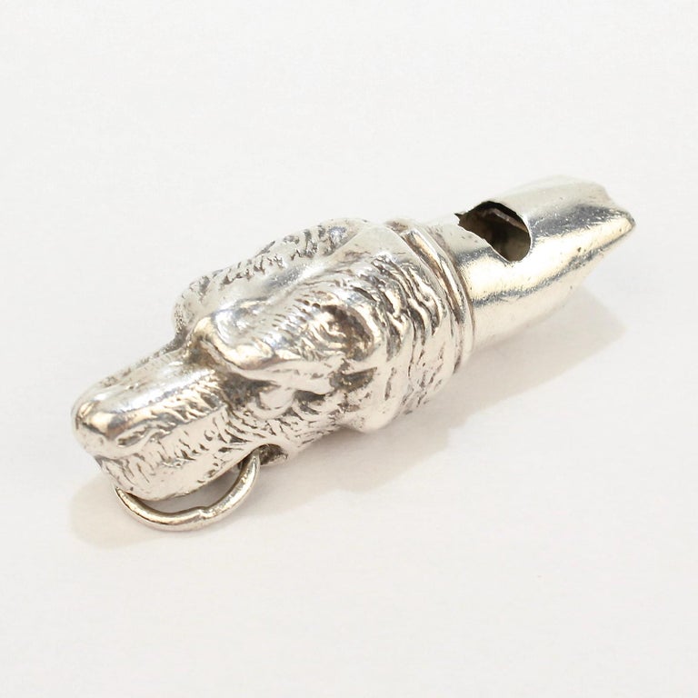 A vintage figural dog whistle in sterling silver.

Made in sterling silver in the form of the bust of a retriever mounted atop a (somewhat) functional whistle.

The dog holds a bail in its mouth so that it can be suspended on a chain or