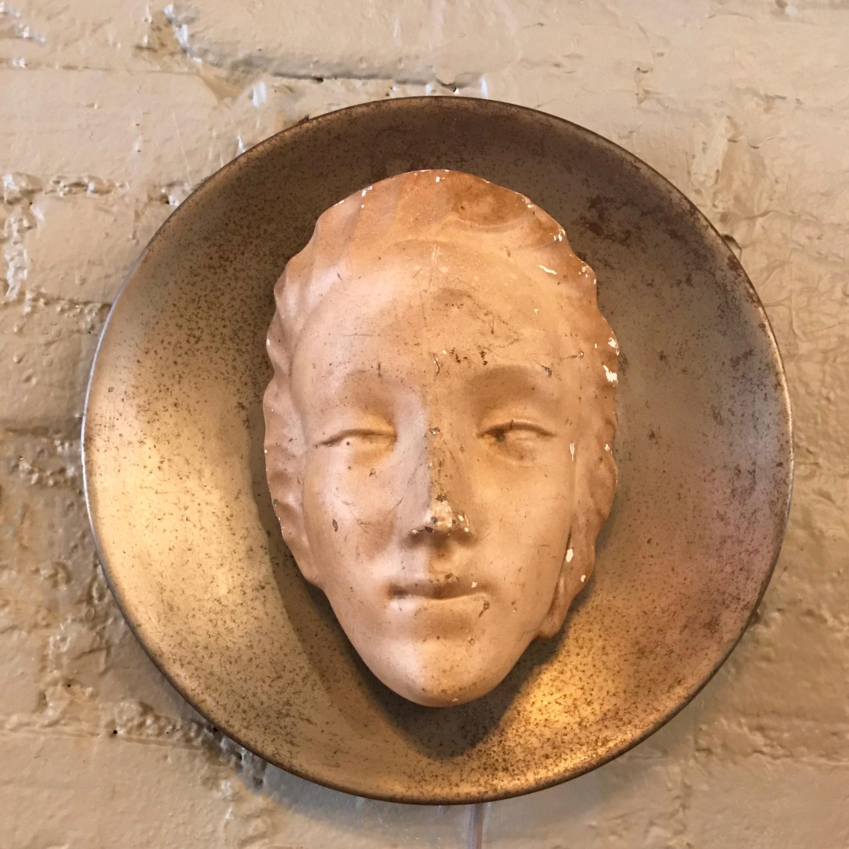 Figurative, Art Deco, wall sconce features a gypsum facial sculpture with a lovely antique patina, back-lit against a steel convex disc.
