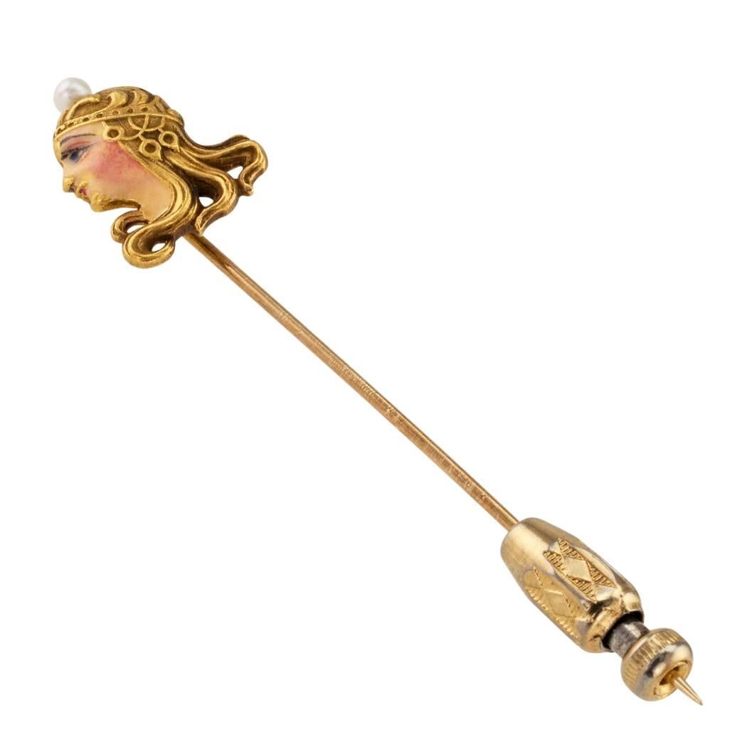 Figurative Art Nouveau 1905 enamel pearl and gold stick pin. Featuring the profile of a classical Art Nouveau female face with long flowing curls adorned by a lavish head dress crowned by a single pearl, the face realistically rendered in blushing