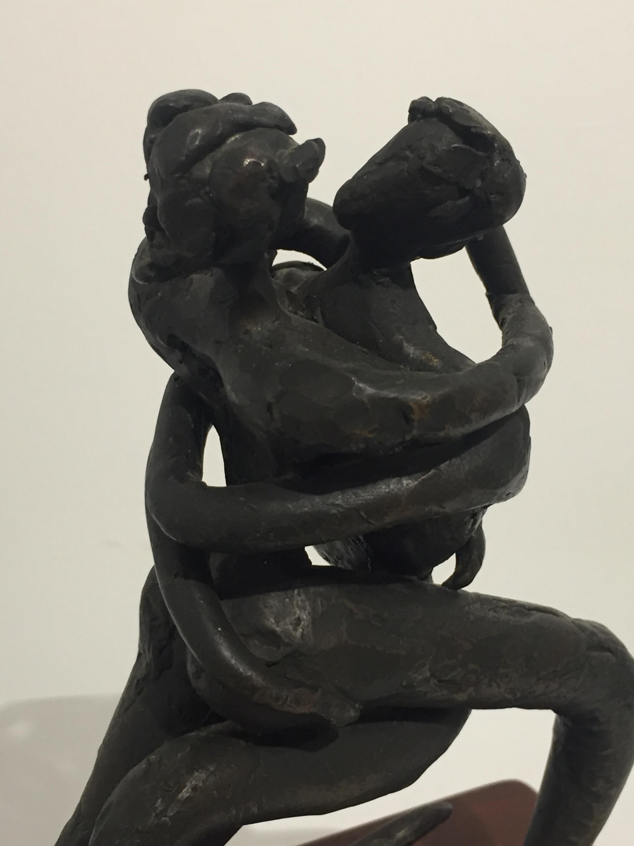 Escultura figurativa de bronce de dos amantes abrazados. La escultura tiene una textura tosca, una pátina oscura y una base de madera.

Medidas
Escultura: 7,5