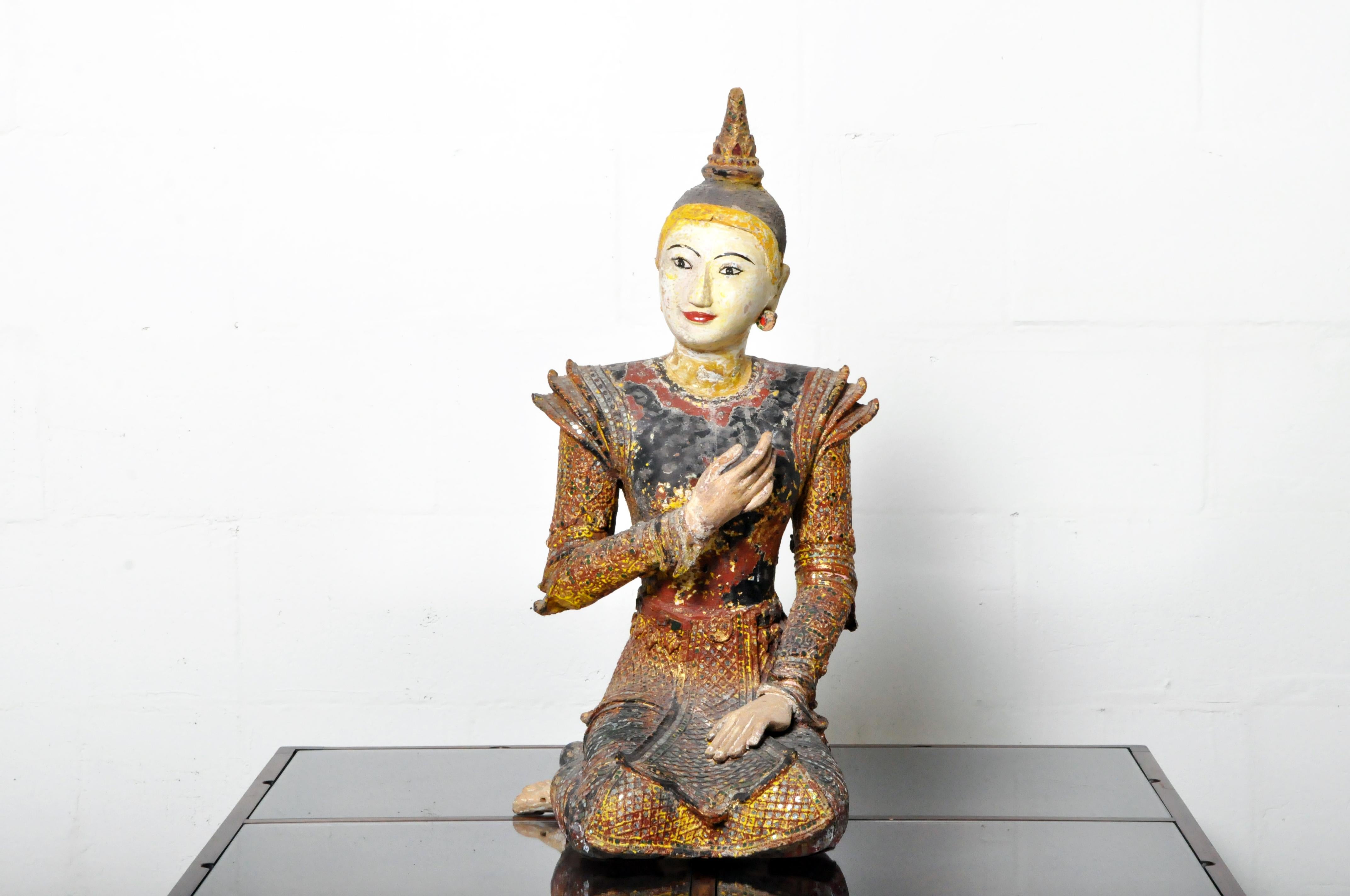 A finely carved wooden sculpture of a Buddhist angel in the Northern Thai style. It is covered in natural lacquer, gold leaf, polychrome, and glass mirror 