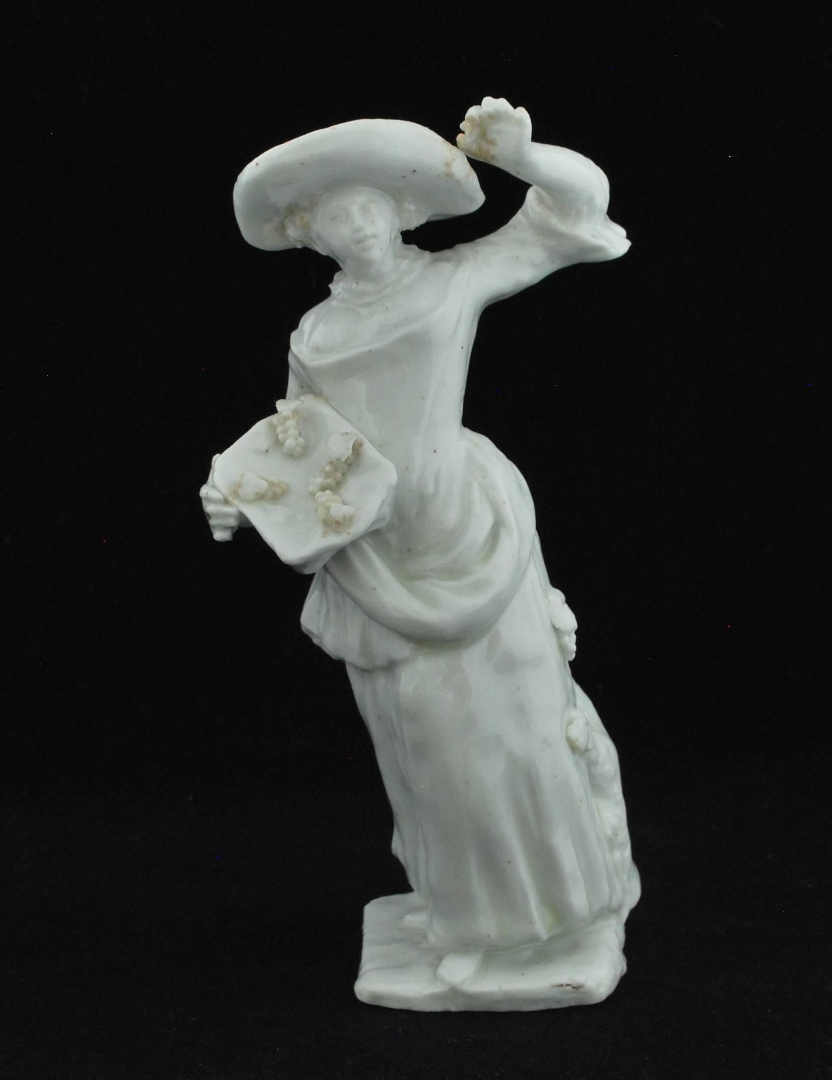 Moulded in a dense body in typical muses modeller style and with slightly drab glaze. She stands by a fruiting vinestock and carries an open basket of grapes in her right hand, her elbow resting on a truncated branch, and raising a bunch of grapes